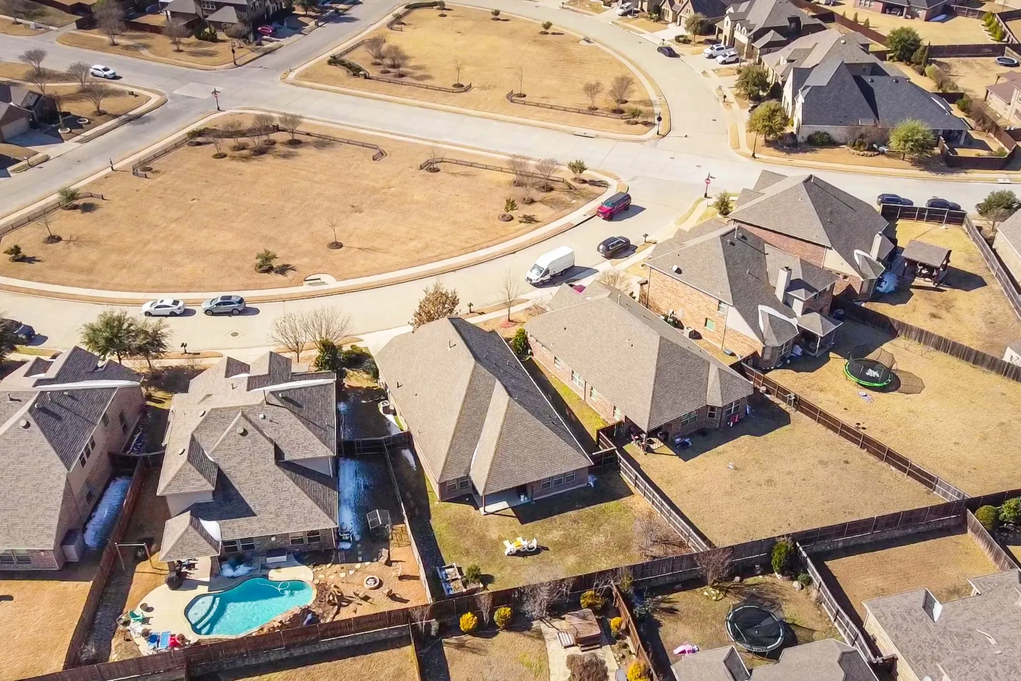 Aerial perspective of a residential corner lot featuring a private in-ground swimming pool, masonry exterior construction, and wood fencing
