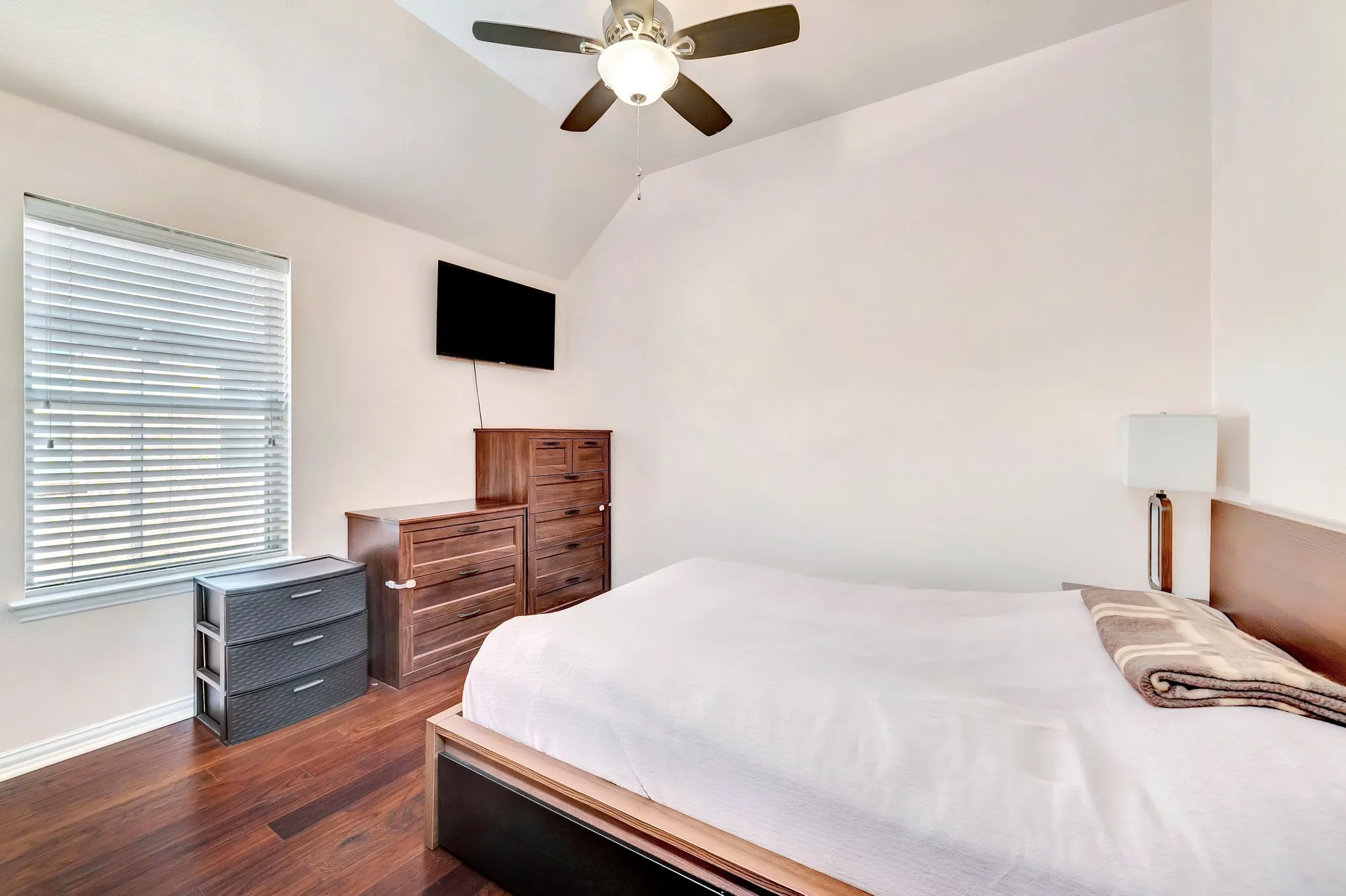 Vaulted ceilings, wood-finish flooring, ceiling fan with integrated lighting, and horizontal window blinds