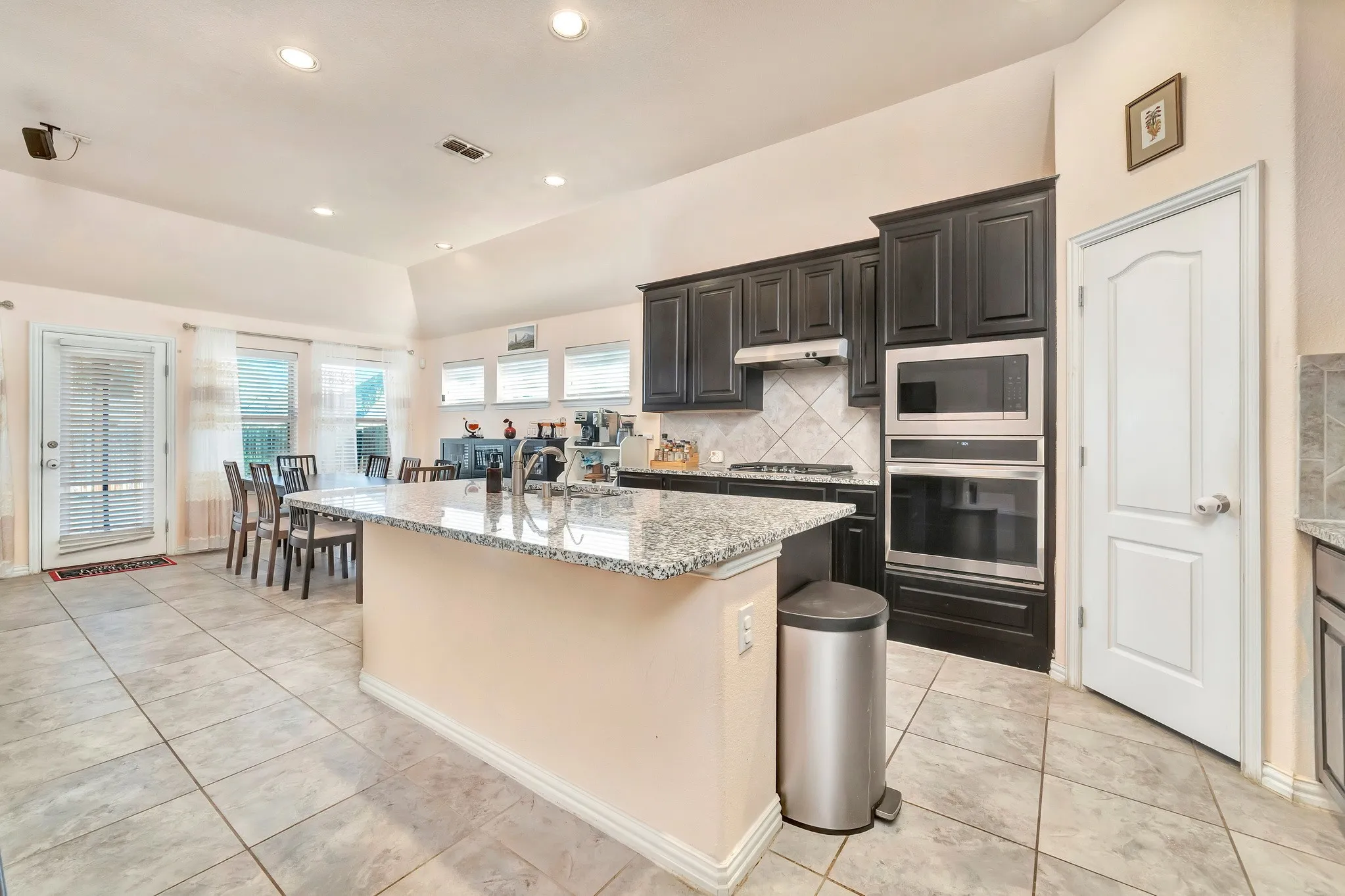 Kitchen featuring stone-finish countertops, dark wood cabinetry, integrated stainless steel double oven, tile backsplash, and ceramic tile flooring