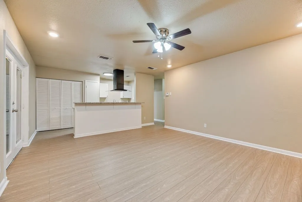 Open-concept space featuring wood-finish flooring, recessed lighting, a ceiling fan, a kitchen island with a stone countertop, and a modern black range hood