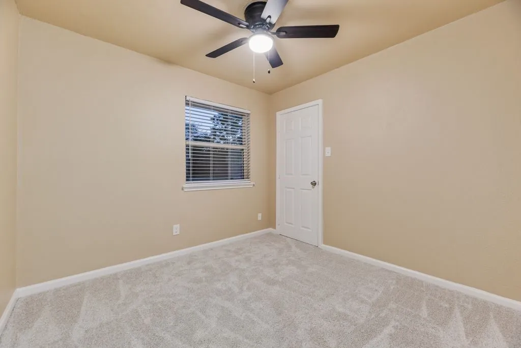 Neutral wall paint, plush carpeting, multi-pane window with horizontal blinds, six-panel interior door, and integrated ceiling fan with light fixture