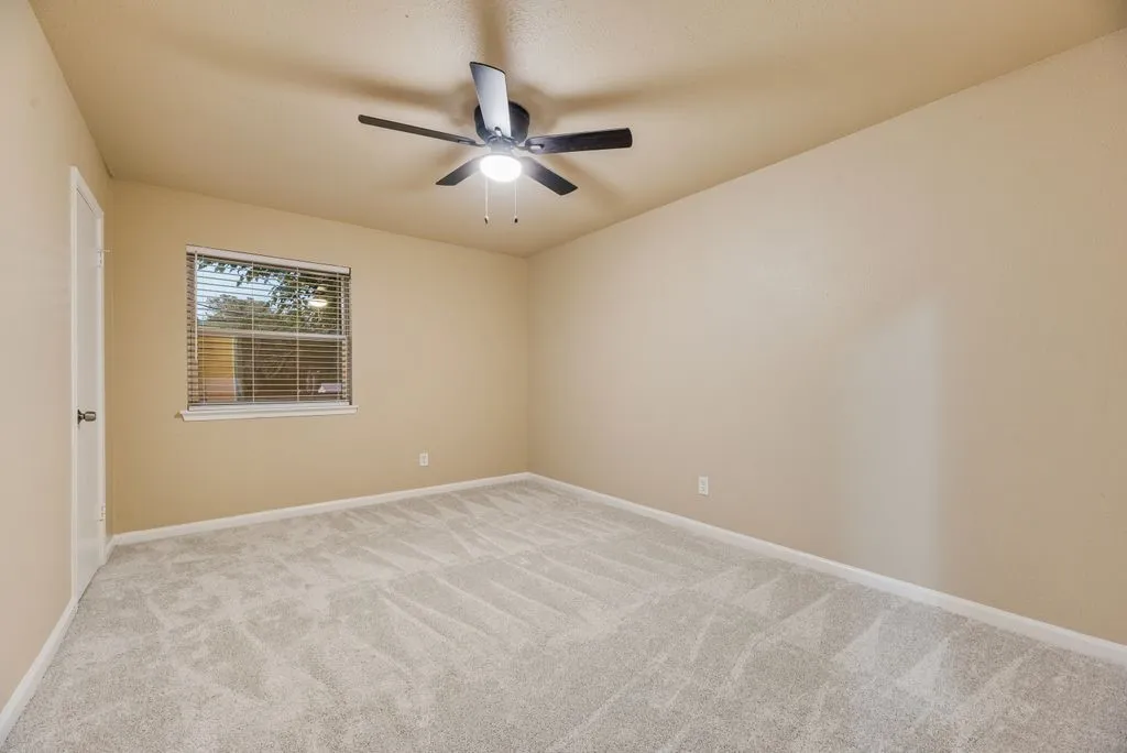 Neutral-toned walls, plush wall-to-wall carpeting, window with slatted blinds, and ceiling fan with integrated light fixture