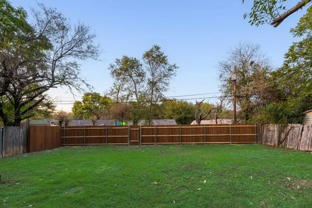 Private backyard featuring a level grass lawn, perimeter wood fencing, and mature trees