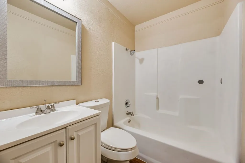 Bathroom featuring a white vanity cabinet with a integrated sink, polished metal faucet, wall-mounted framed mirror, and a white tub-shower combination with surround