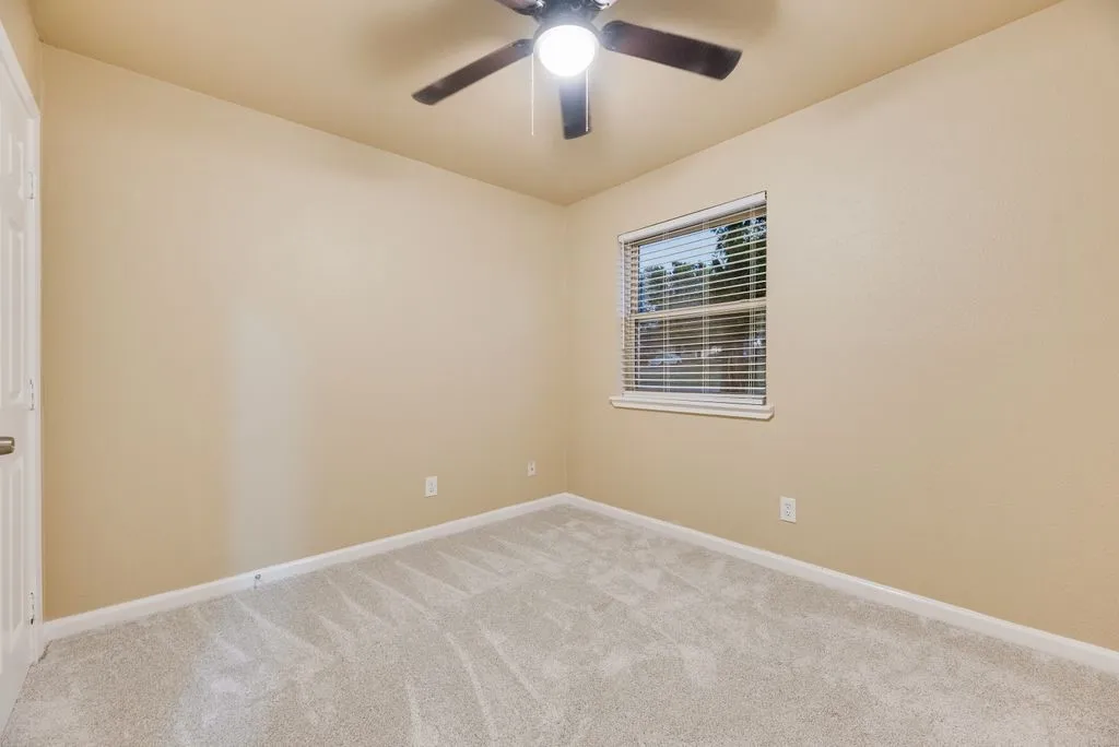 Neutral-toned interior featuring wall-to-wall carpeting, a multi-blade ceiling fan with integrated lighting, and a single-hung window with horizontal blinds