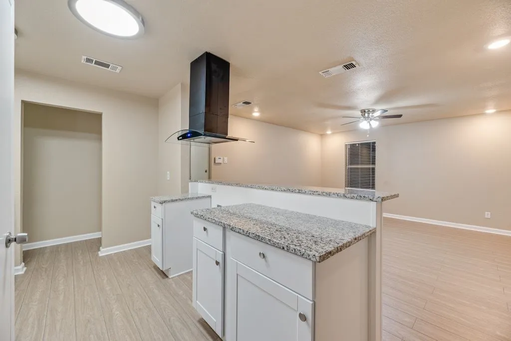 Kitchen featuring white shaker-style cabinetry, stone-finish countertops, stainless steel chimney-style range hood, and wood-finish flooring