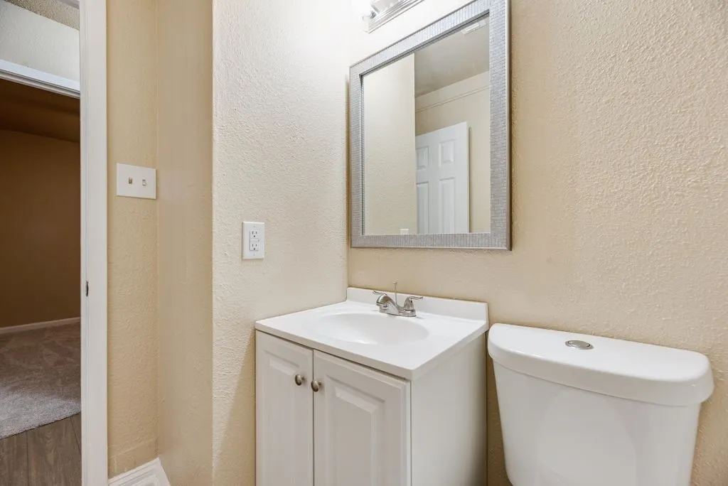 White vanity cabinet with an integrated basin, chrome-finished faucet, framed wall mirror, and dual-flush toilet