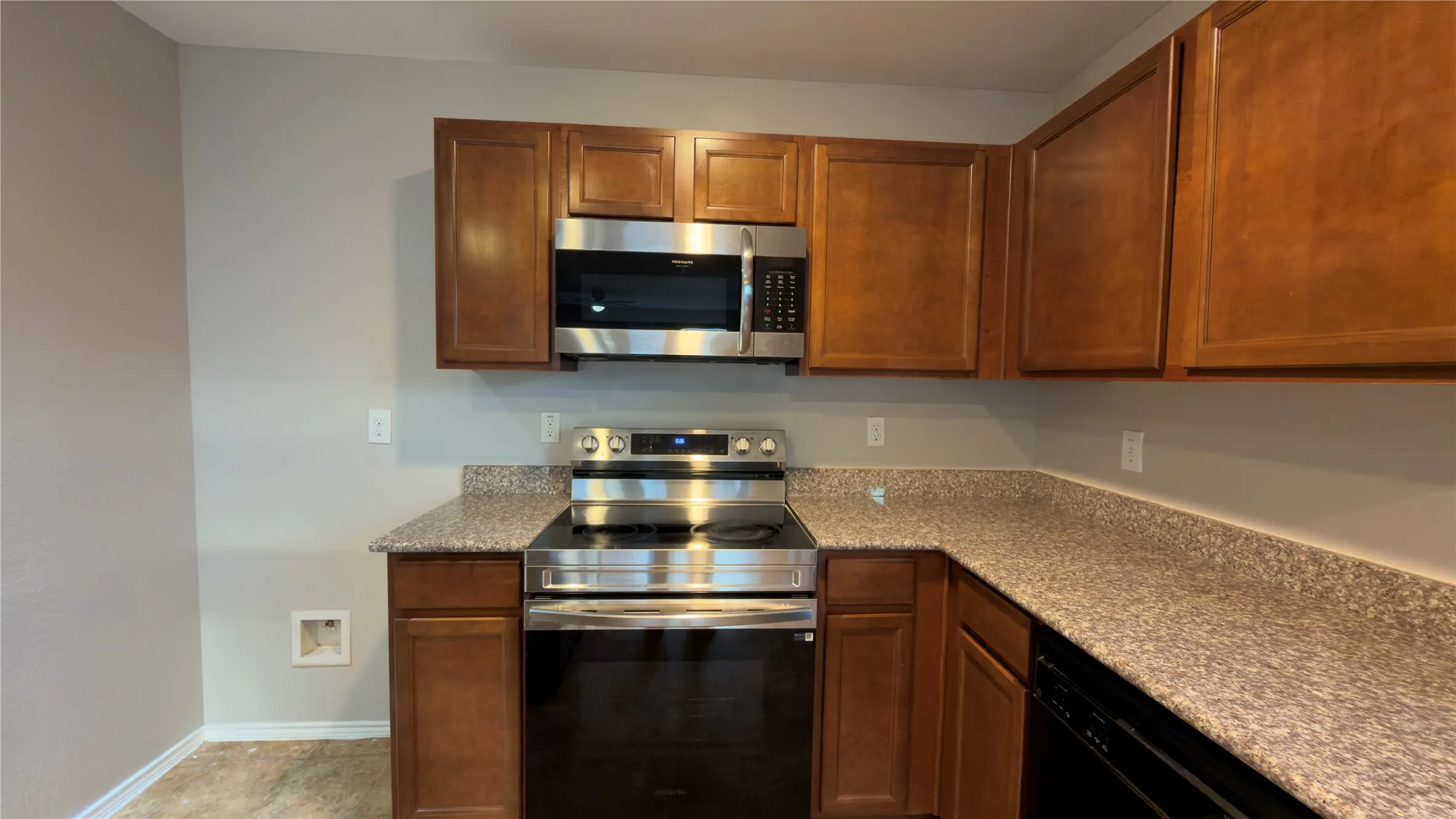 Kitchen featuring stained wood cabinetry, stone-finish countertops, and stainless steel appliances including a built-in microwave and range