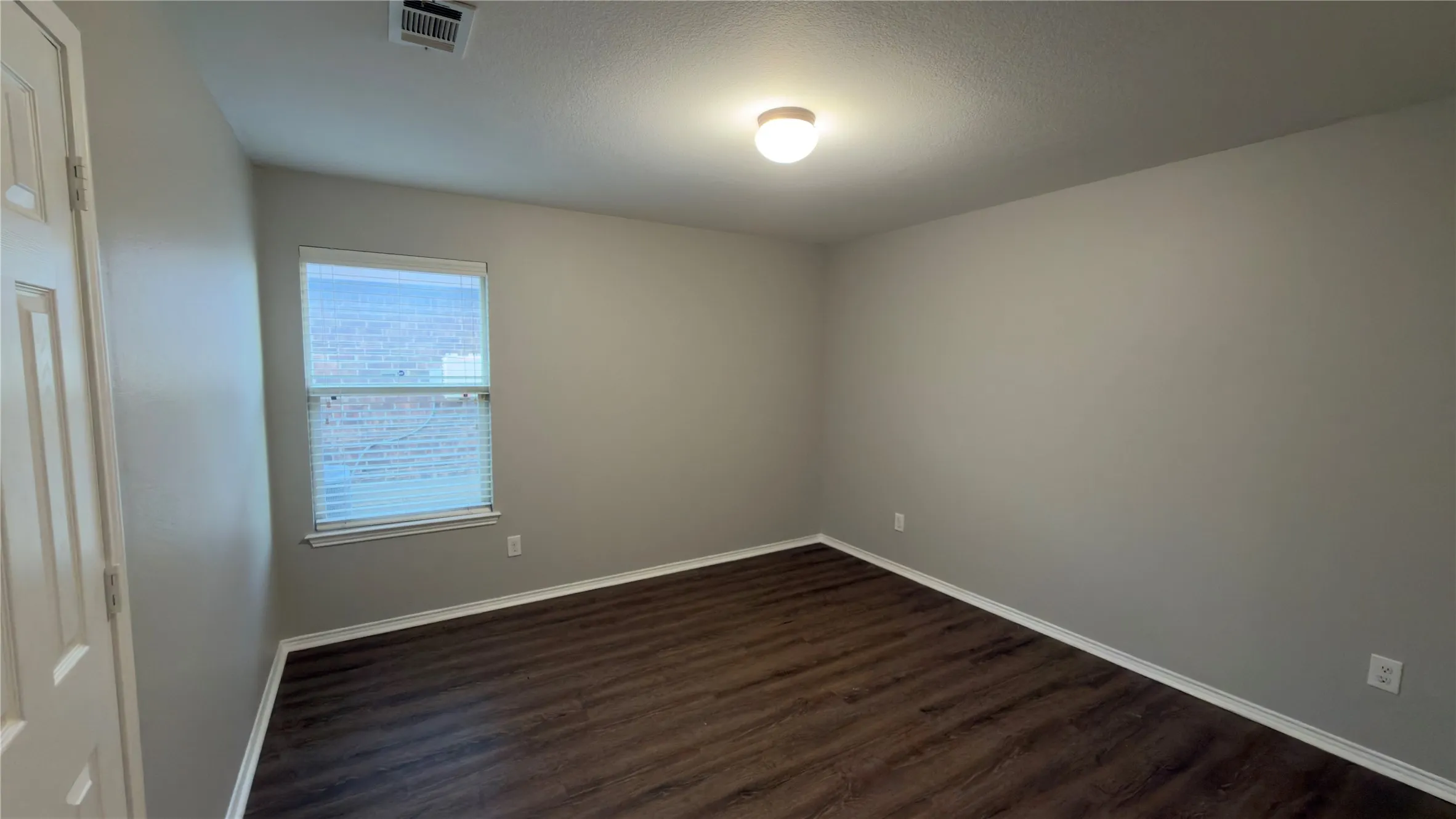 Room featuring wood-finish flooring, neutral wall paint, a single window with blinds, and a ceiling-mounted light fixture