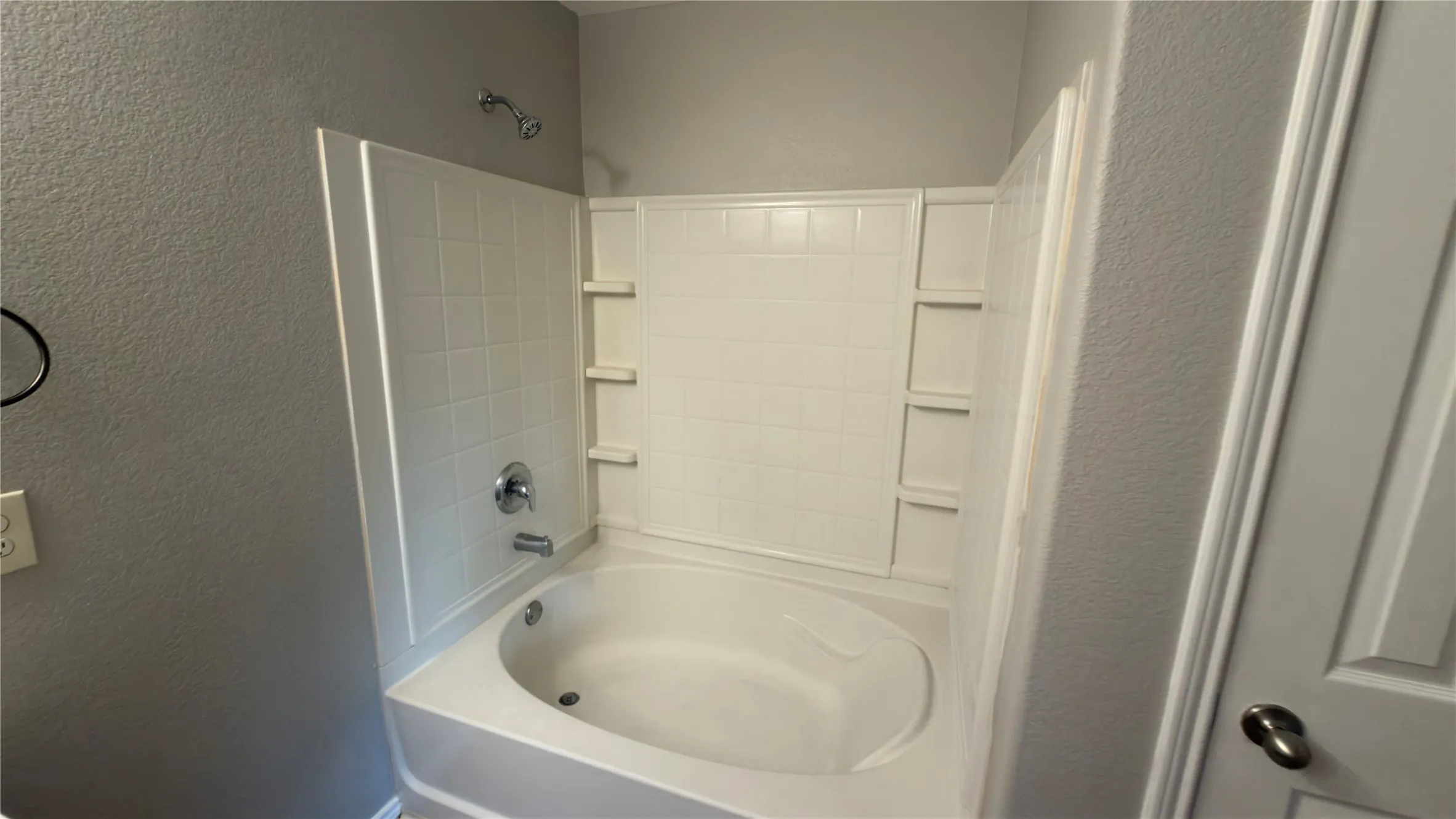 Built-in deep soaking tub with integrated shower head, tiled wall surround, and multiple recessed storage niches