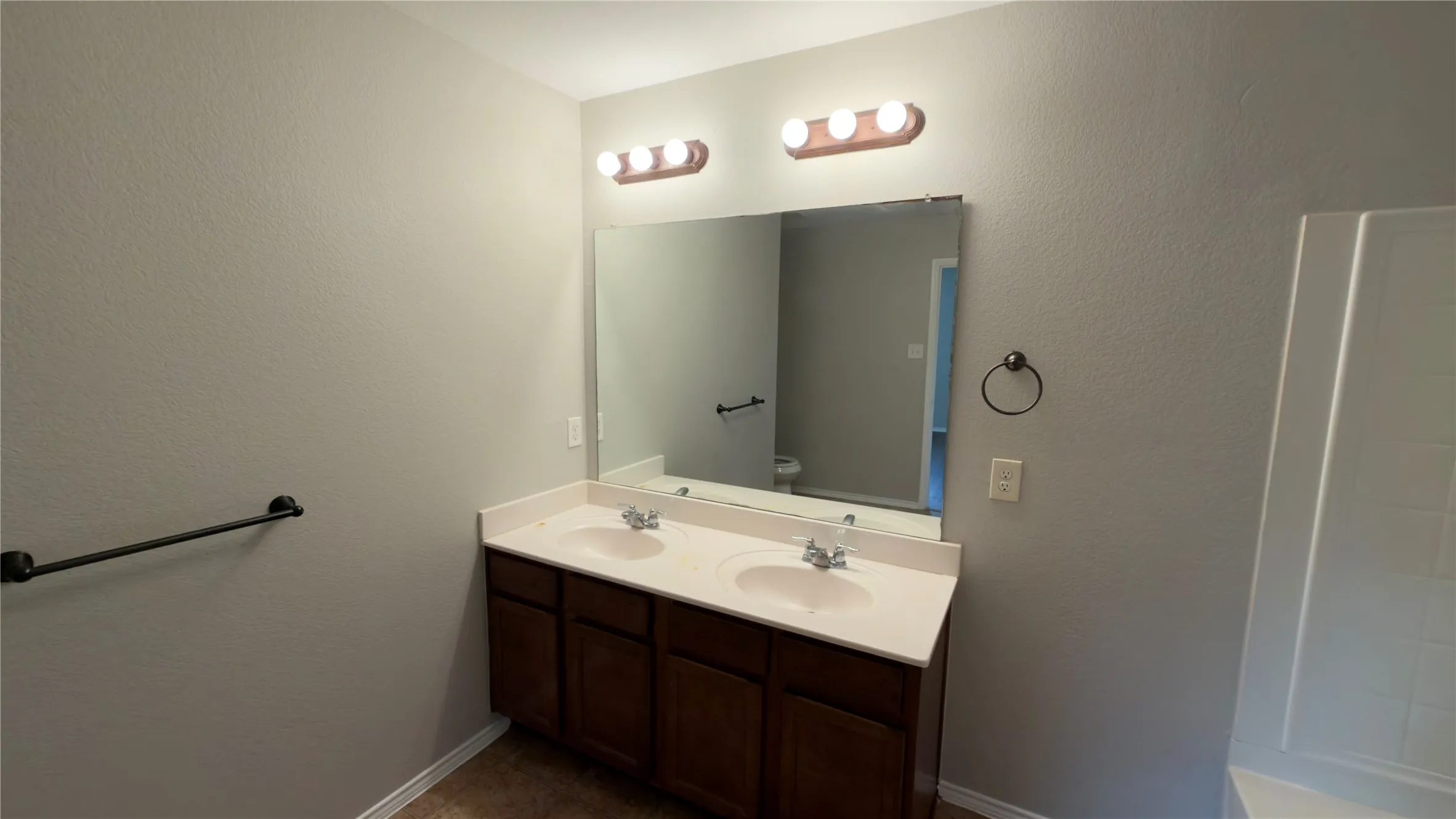 Double-vanity cabinet with a white countertop, dual integrated sinks, wall-to-wall mirror, and dark-finish hardware