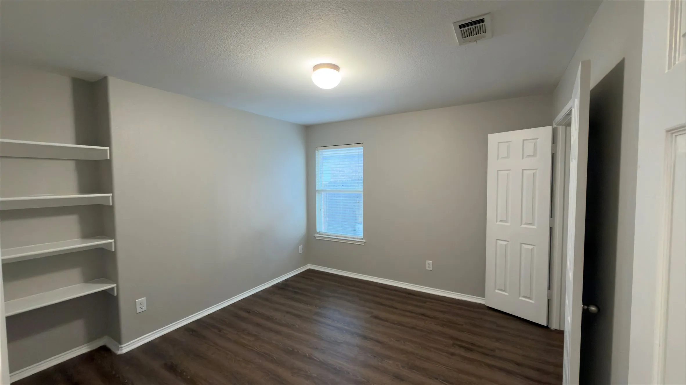 Interior room featuring wood-finish flooring, built-in shelving, a recessed window, and a six-panel door