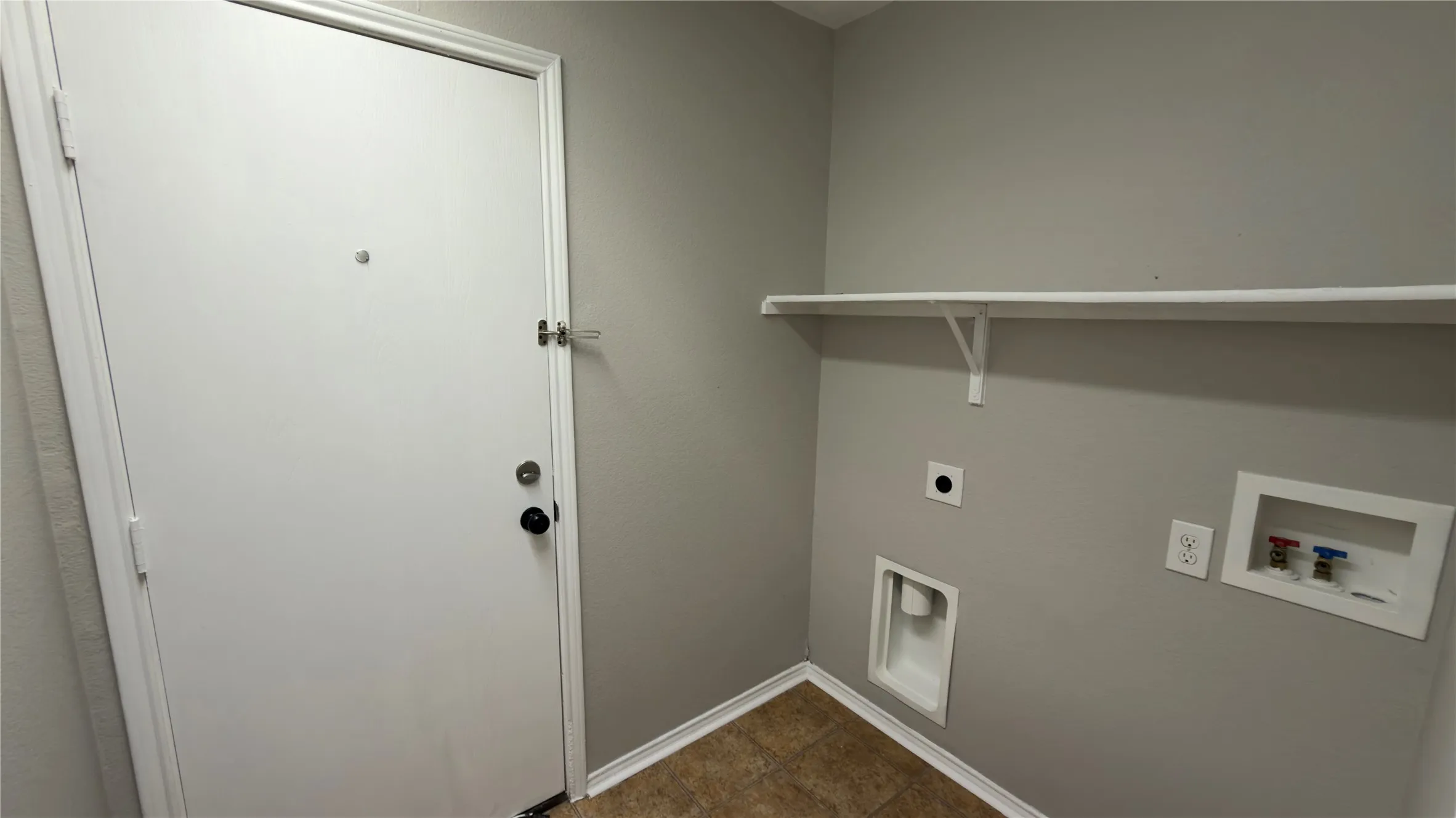 Utility area featuring neutral wall paint, tiled flooring, an installed shelf, and dedicated water and electrical hookups