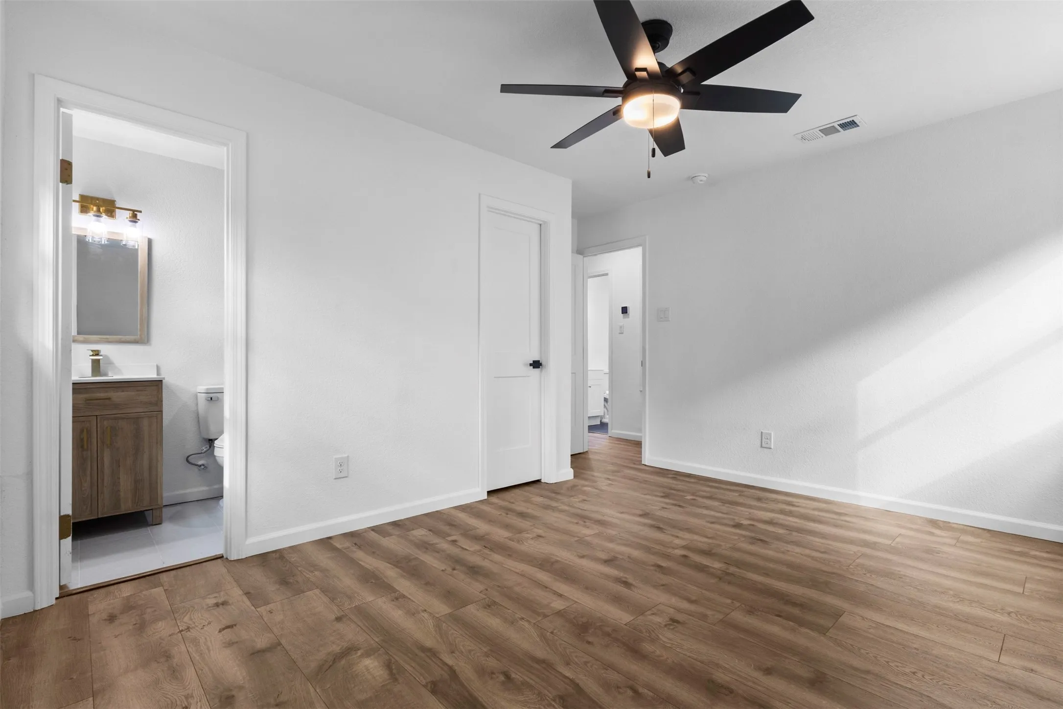 Wood-finish flooring, matte black ceiling fan with integrated lighting, and solid core interior doors