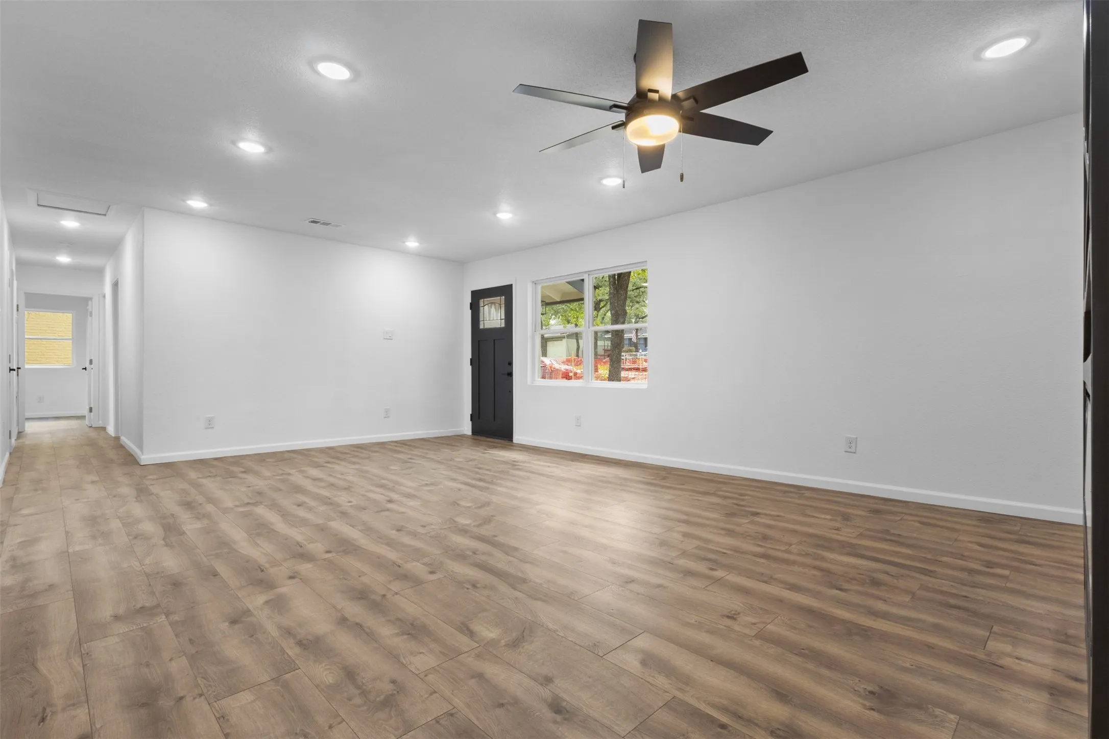 Open-concept room featuring wood-finish flooring, recessed lighting, a modern ceiling fan with integrated lighting, and a dark-finish exterior door with a decorative glass panel