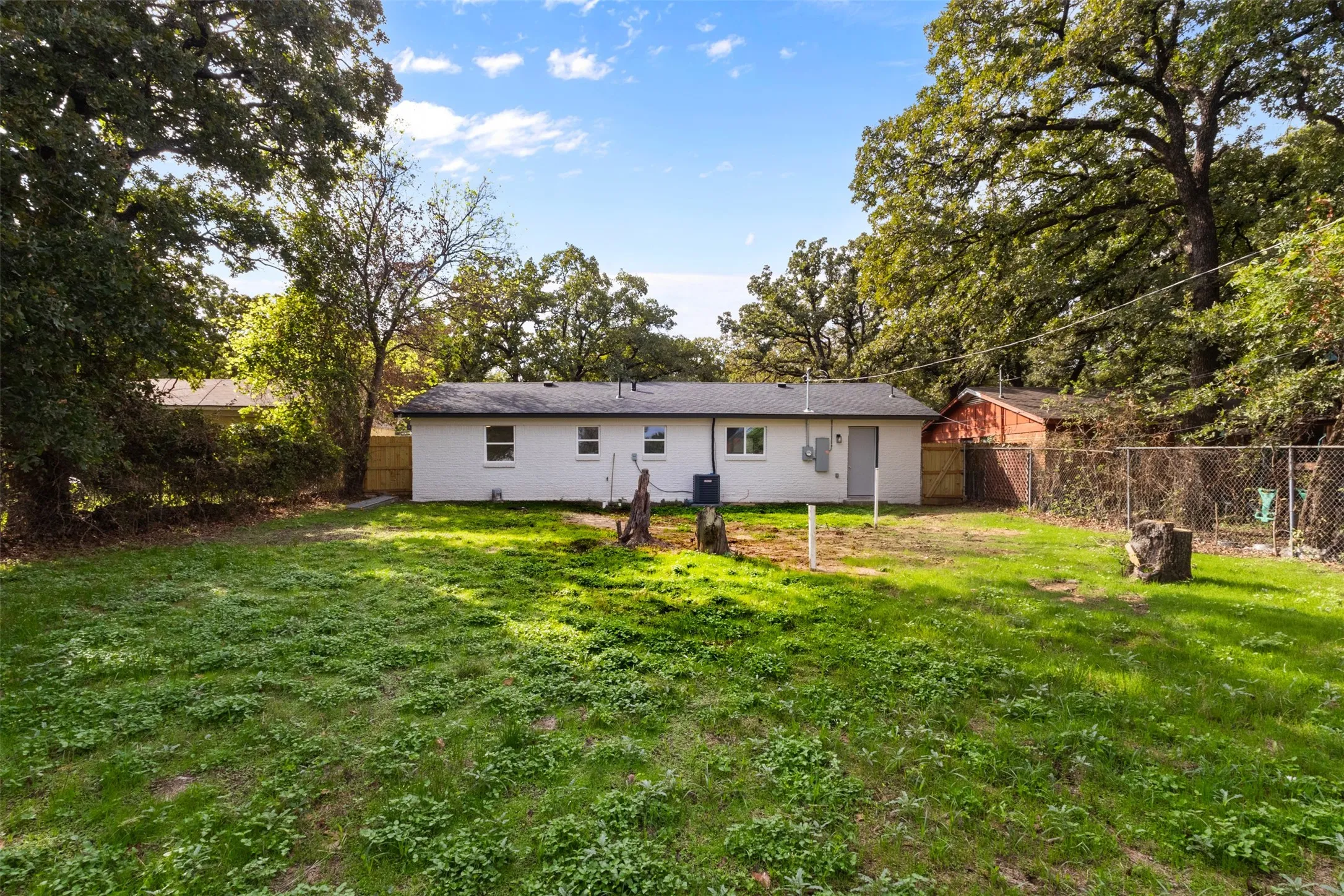 Expansive backyard featuring mature trees, a white painted brick exterior, and wood privacy fencing