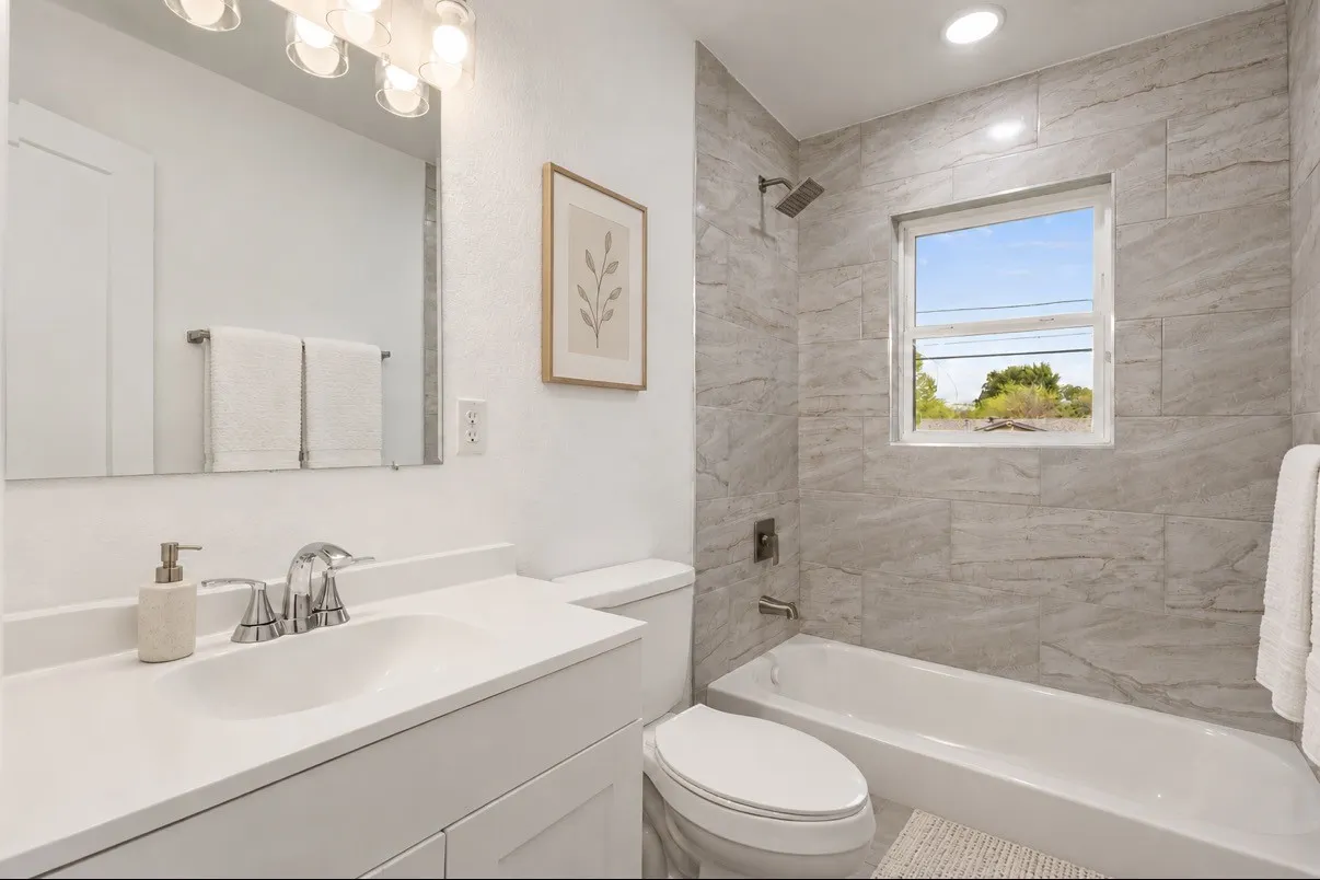 Bathroom featuring a white vanity with a rectangular basin, large wall-mounted mirror, recessed lighting, and a shower-tub combination with horizontal stone-finish tile surround and metallic hardware