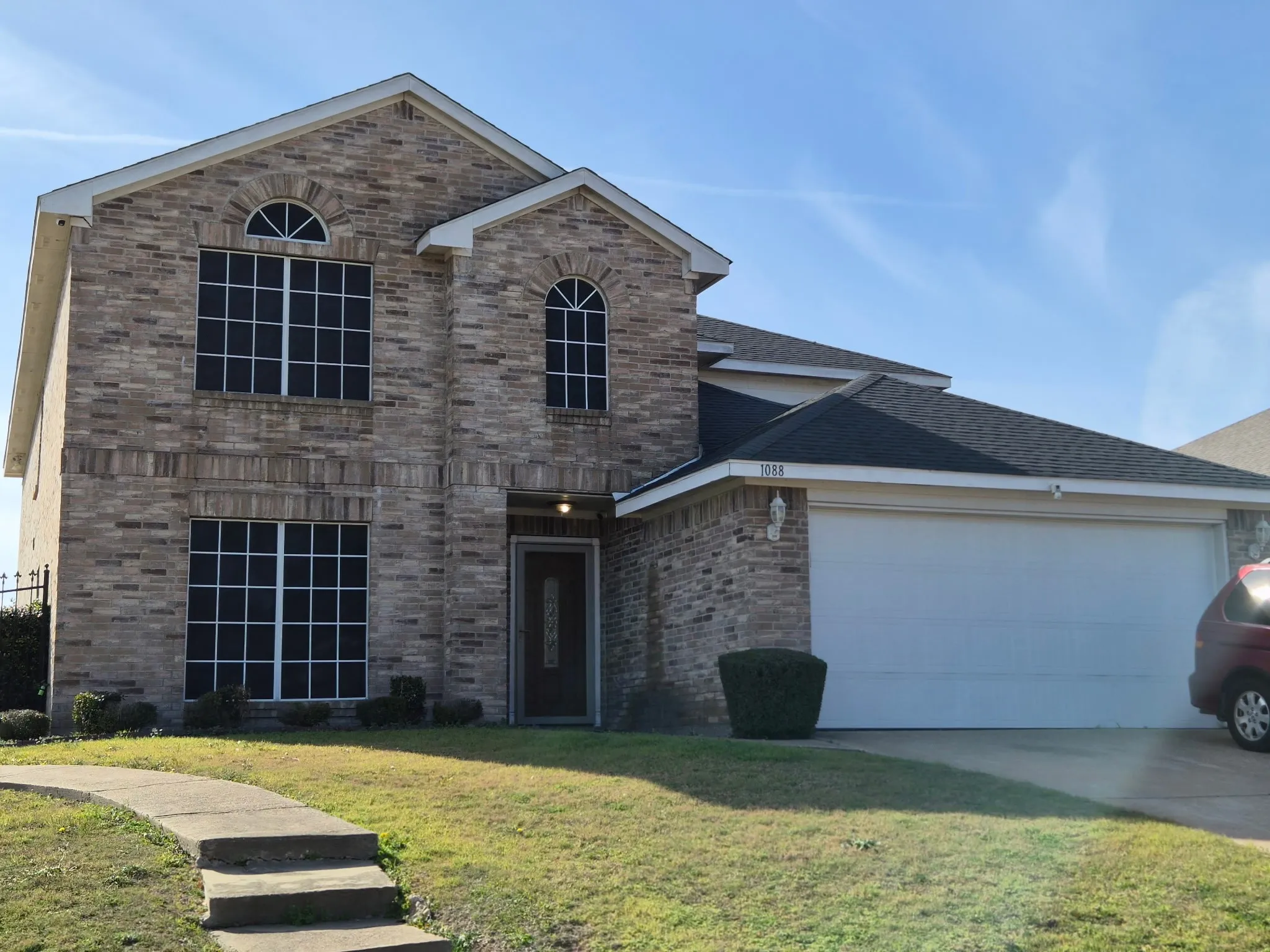 Two-story brick exterior featuring an arched window, decorative gables, an attached two-car garage, and concrete walkway