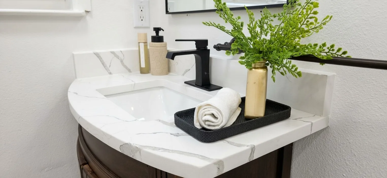 Curved vanity featuring a white surface with grey veining, integrated basin, matte black faucet, and framed mirror