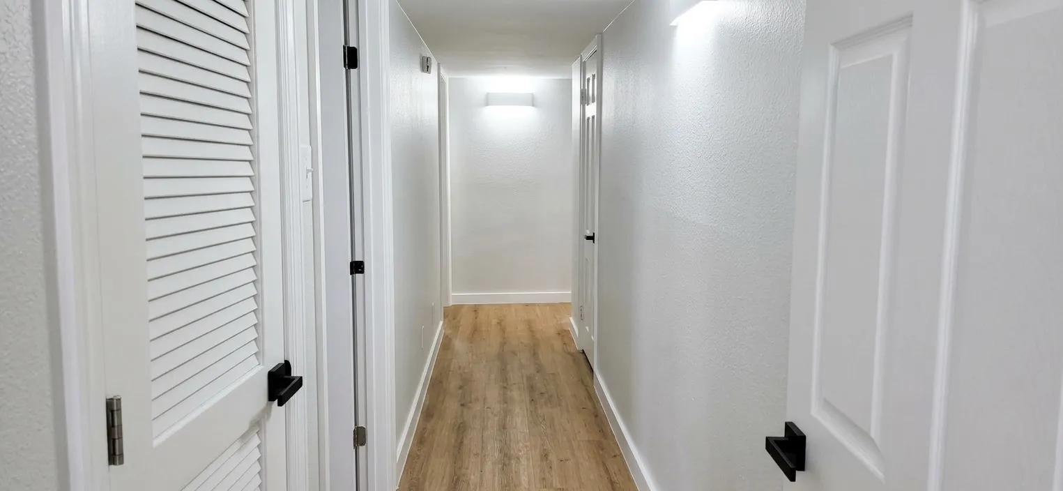 Hallway featuring wood-finish flooring, white panel doors, louvered closet door, and matte black door hardware