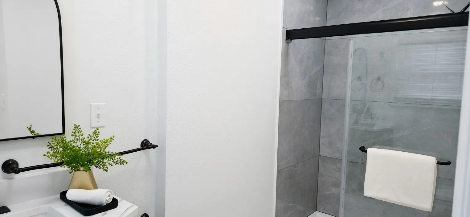 Bathroom featuring a walk-in shower with large-format grey tile surround, black frame sliding glass enclosure, arched wall mirror, and matte black hardware