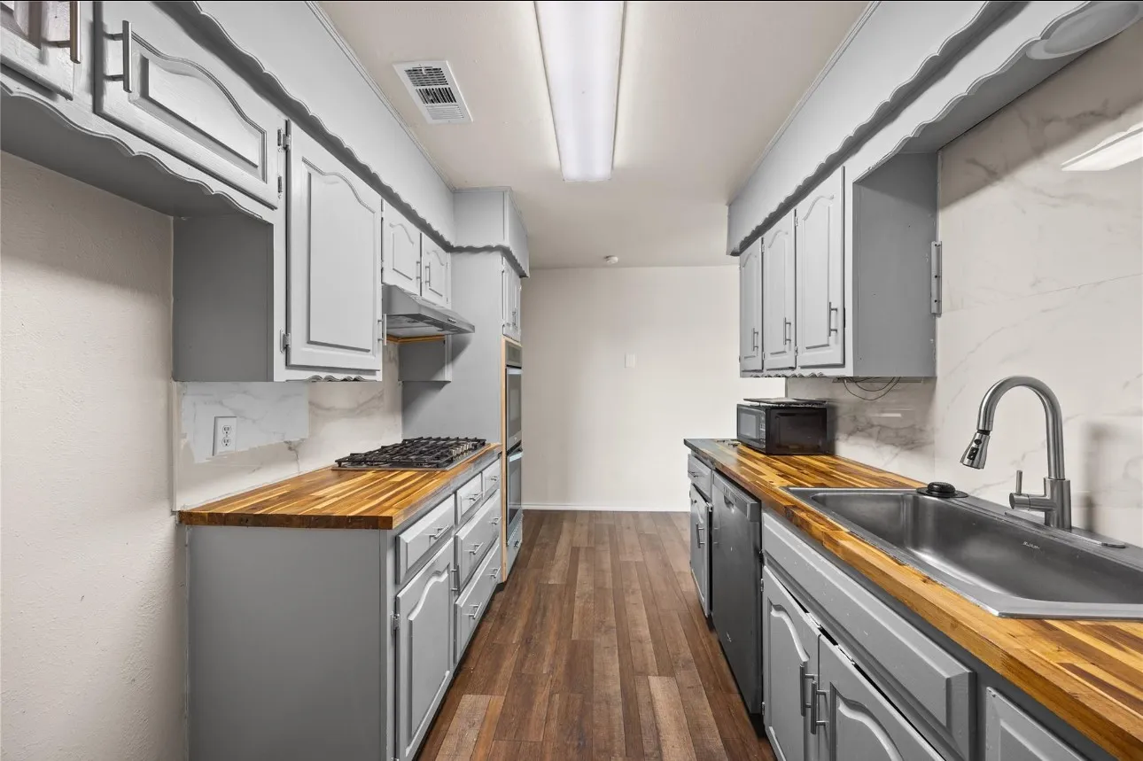 Kitchen featuring light gray cabinetry, butcher block countertops, white stone-finish backsplash, stainless steel gas cooktop, and wood-finish flooring