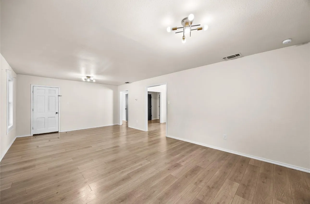 Neutral-toned interior space featuring wood-finish flooring, multi-directional ceiling light fixtures, and a six-panel door