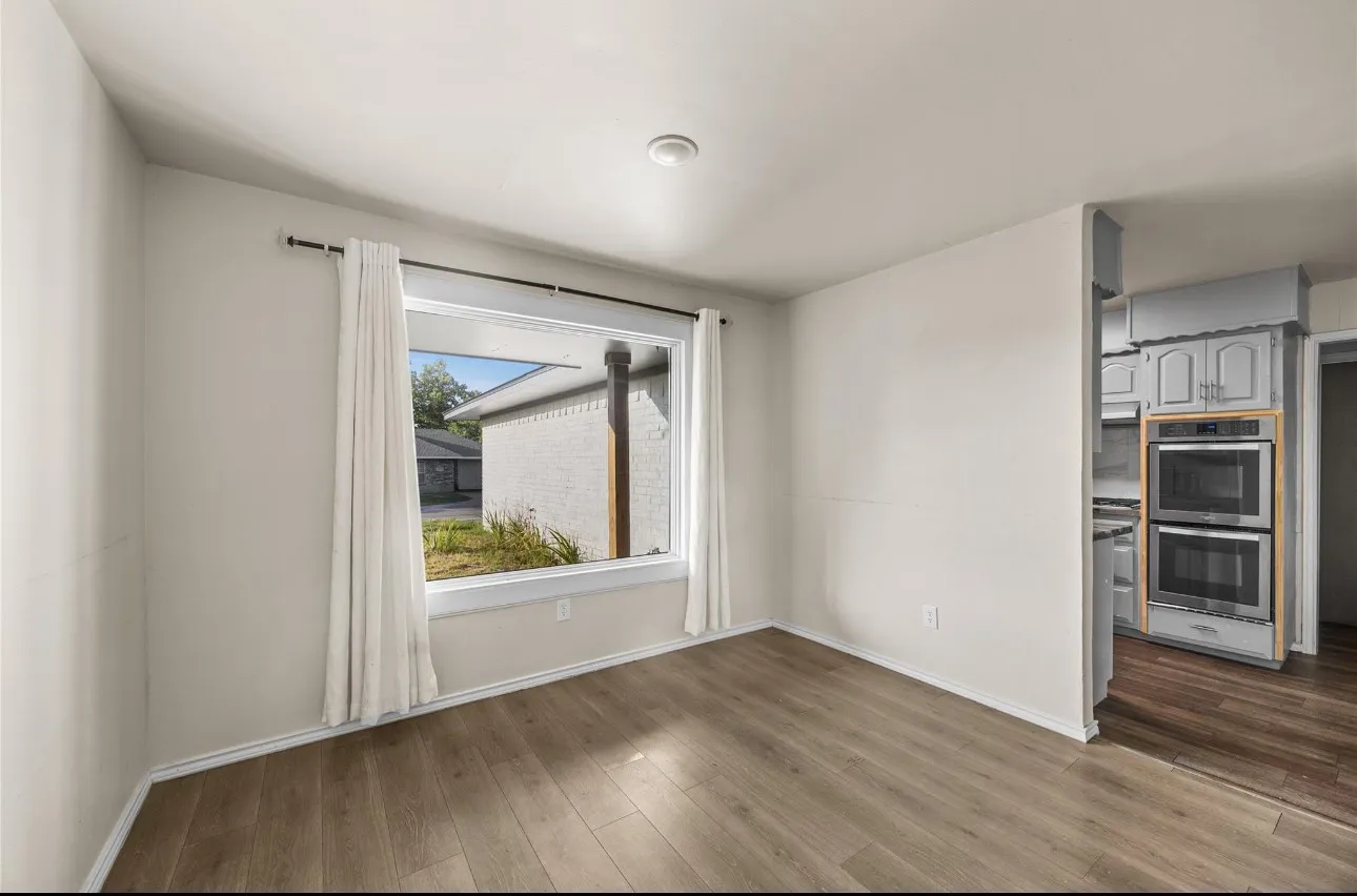 Room featuring wood-finish flooring, a large picture window, and recessed lighting, with a built-in stainless steel double oven in the kitchen