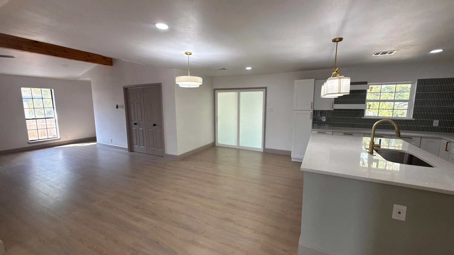 Open-concept kitchen featuring an island with a light-toned countertop, custom cabinetry, tiled backsplash, wood-finish flooring, and exposed ceiling beams