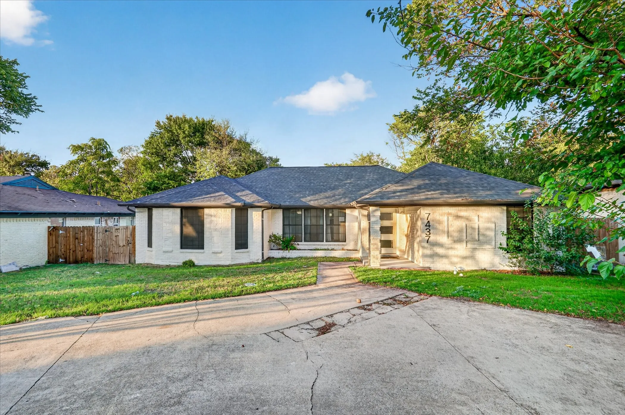 Single-story residence with painted brick exterior, shingled hip roof, grid-pattern windows, and concrete driveway