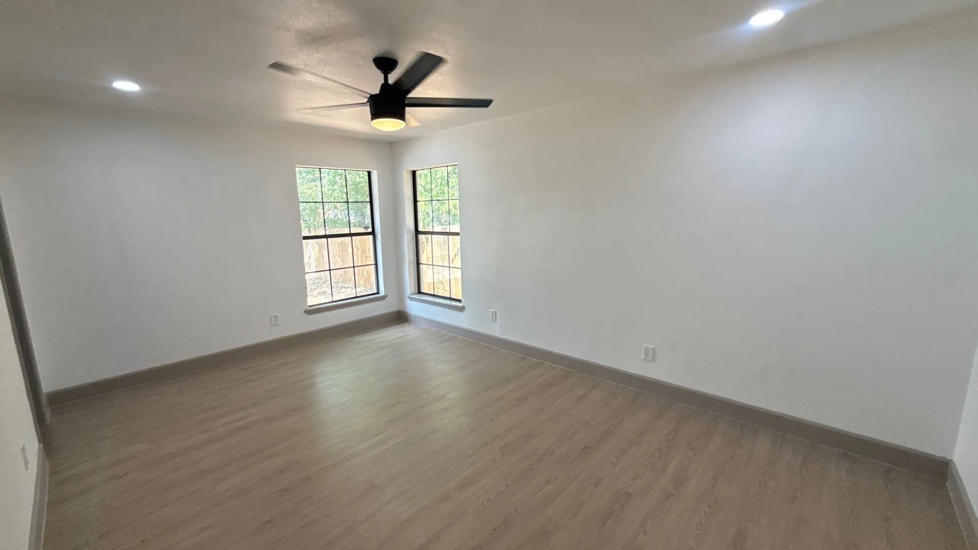 Neutral-toned room featuring wood-finish flooring, recessed lighting, a ceiling fan, and multi-pane windows with dark frames