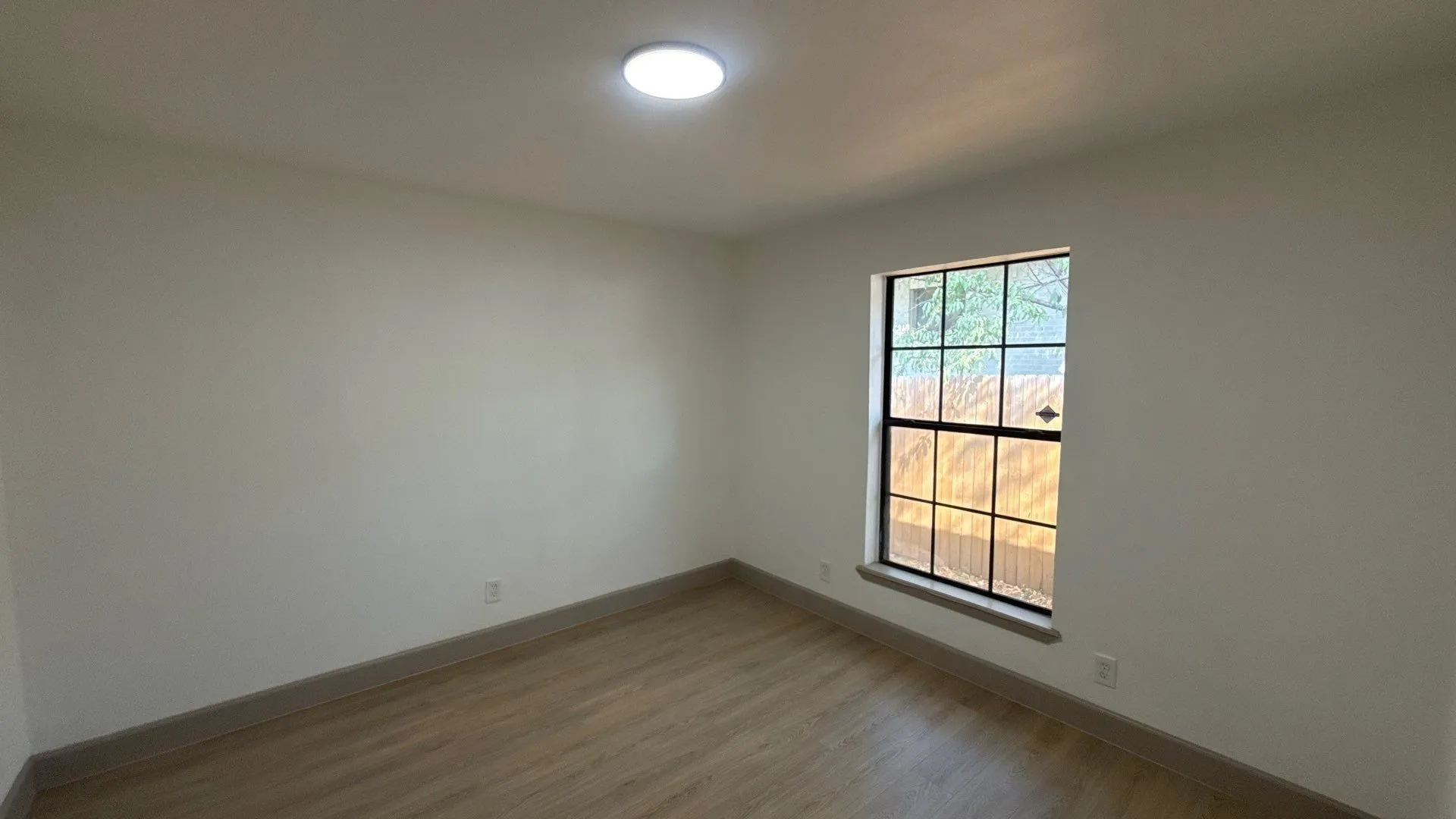 Interior space featuring neutral wall paint, wood-finish flooring, a grid-pattern window, and a flush-mount ceiling light fixture