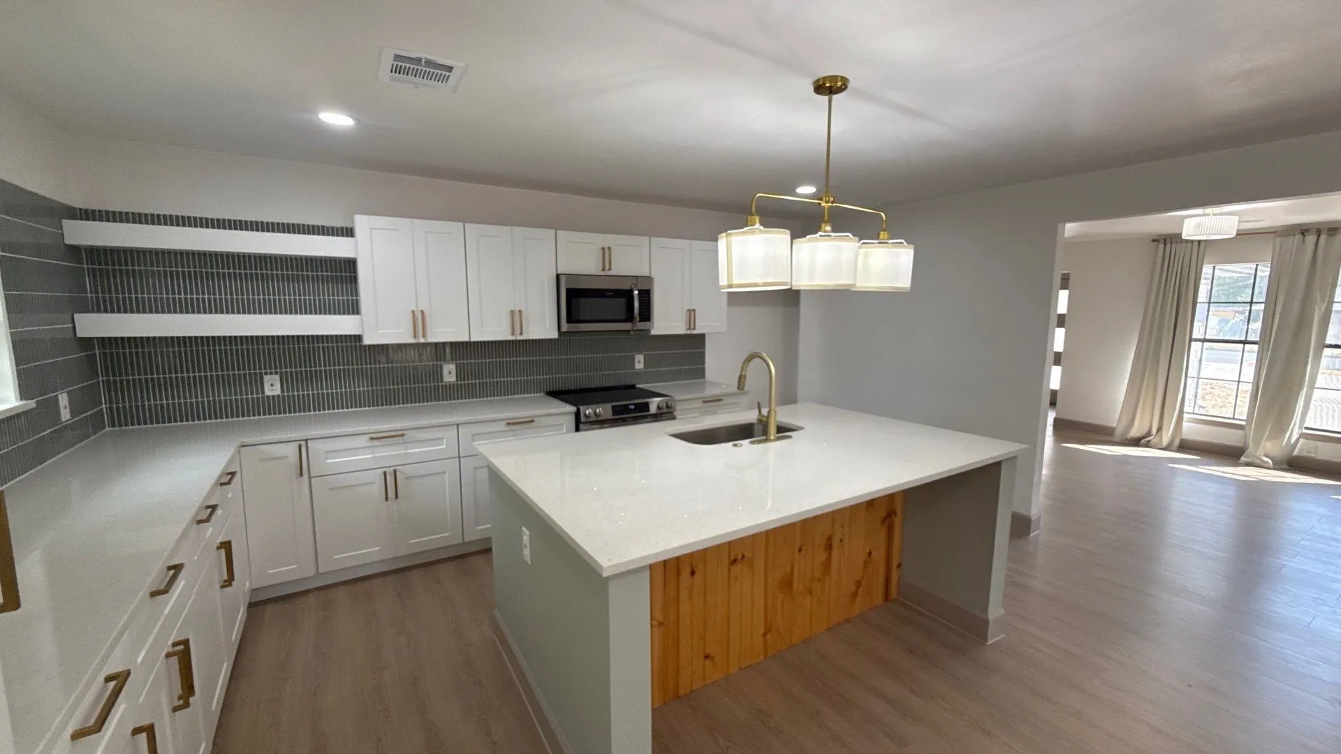 Kitchen featuring white shaker-style cabinetry, a central island with wood-paneling detail, quartz countertops, a linear tile backsplash, and metallic hardware
