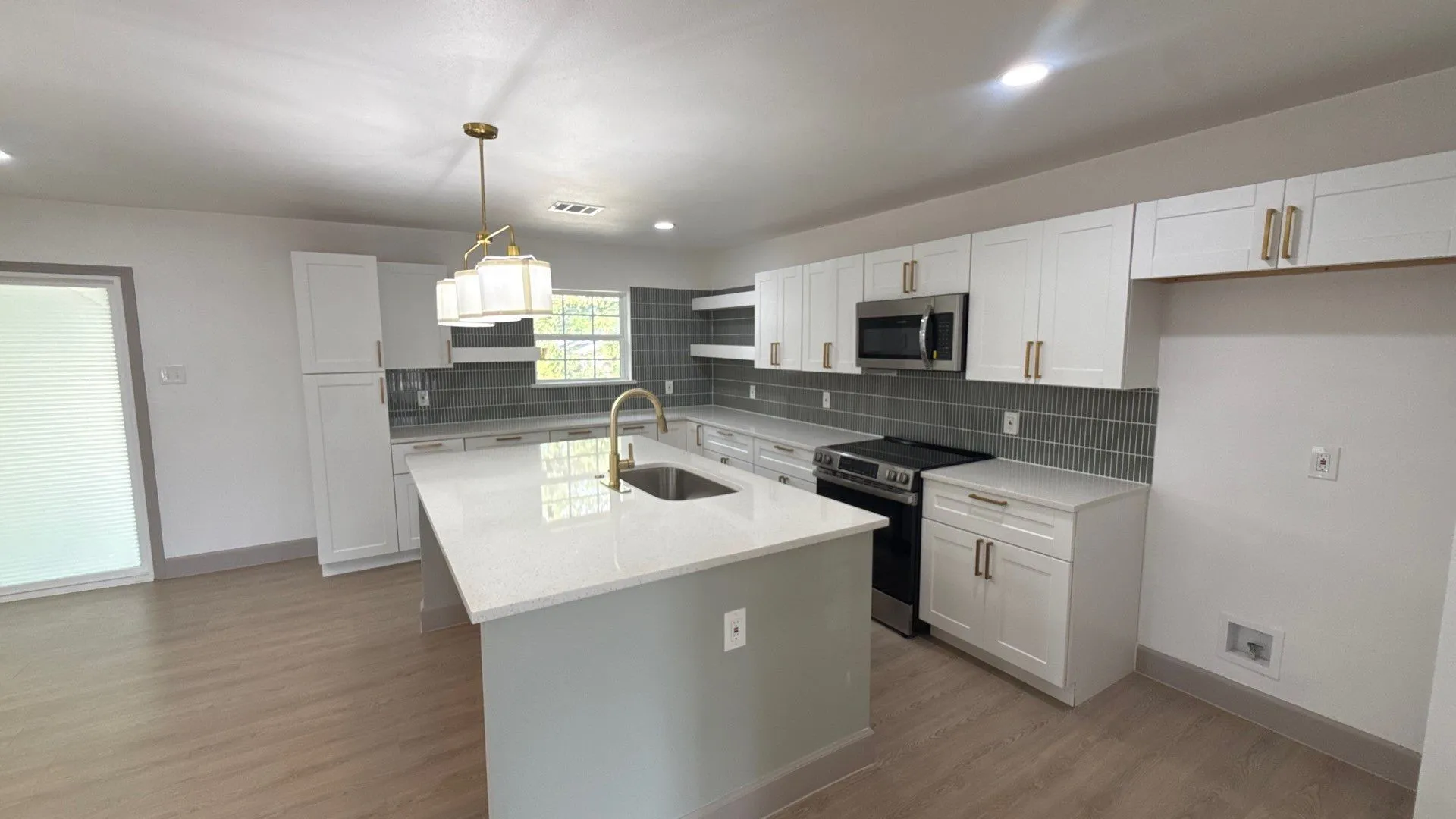 Kitchen featuring white shaker cabinetry, quartz countertops, a central island with a stainless steel undermount sink, a tiled backsplash, and wood-finish flooring