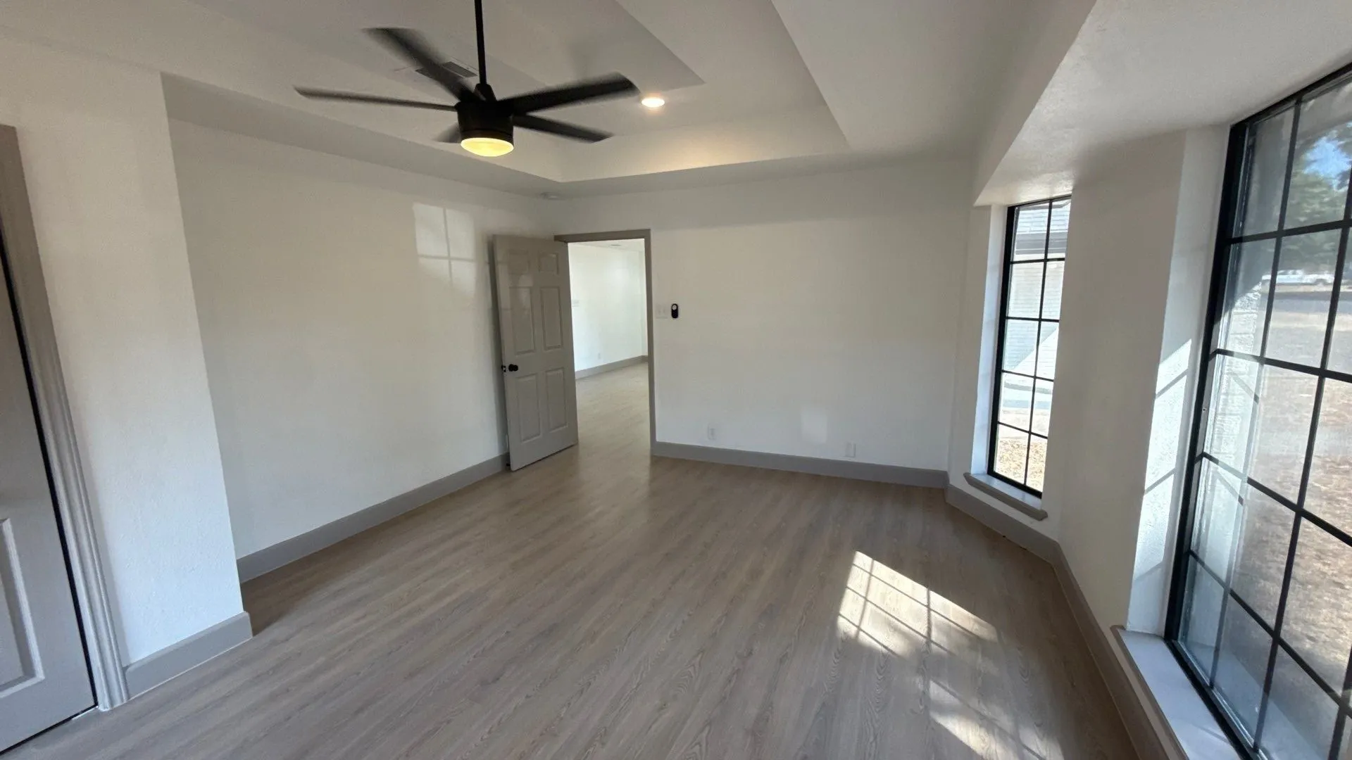 Interior space featuring wood-finish flooring, a tray ceiling with a matte black ceiling fan, and large windows with black mullions