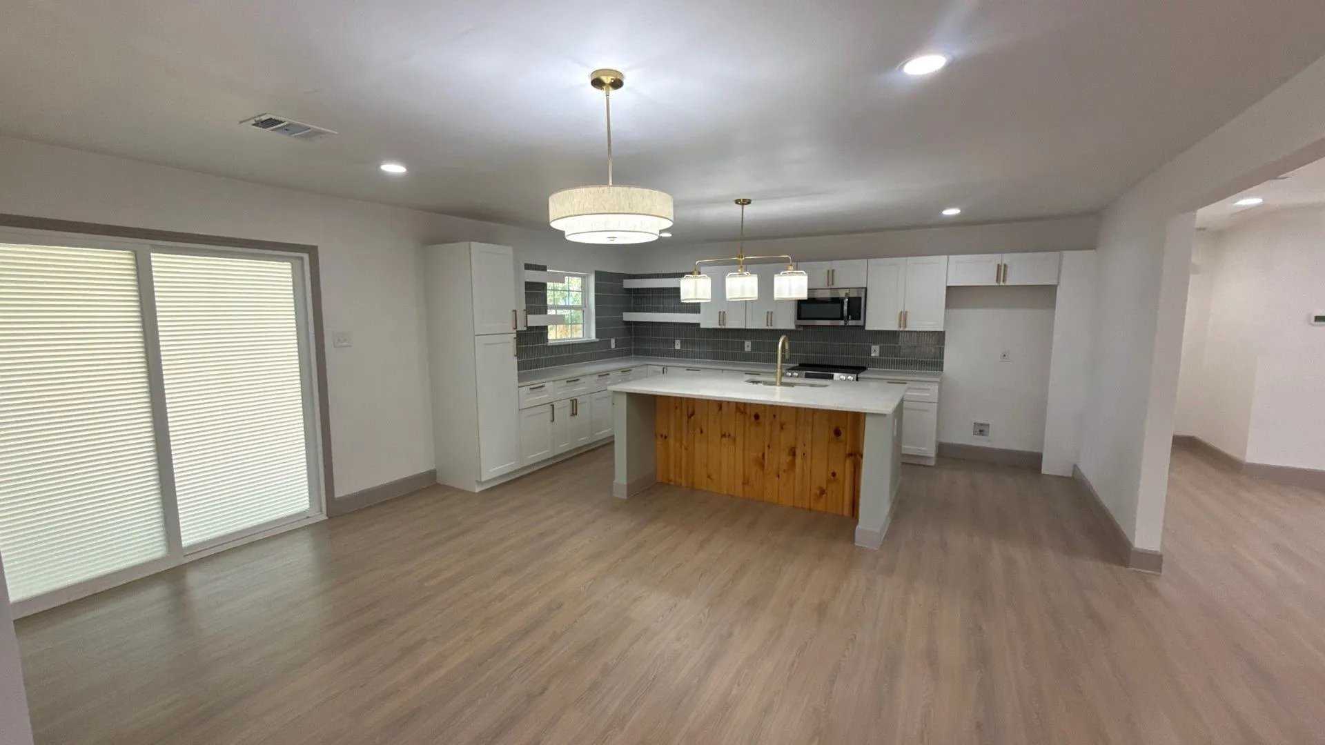 Kitchen featuring wood-finish flooring, a central island with a wood-paneled base and solid surface countertop, white shaker-style cabinetry, a tile backsplash, and recessed and pendant lighting
