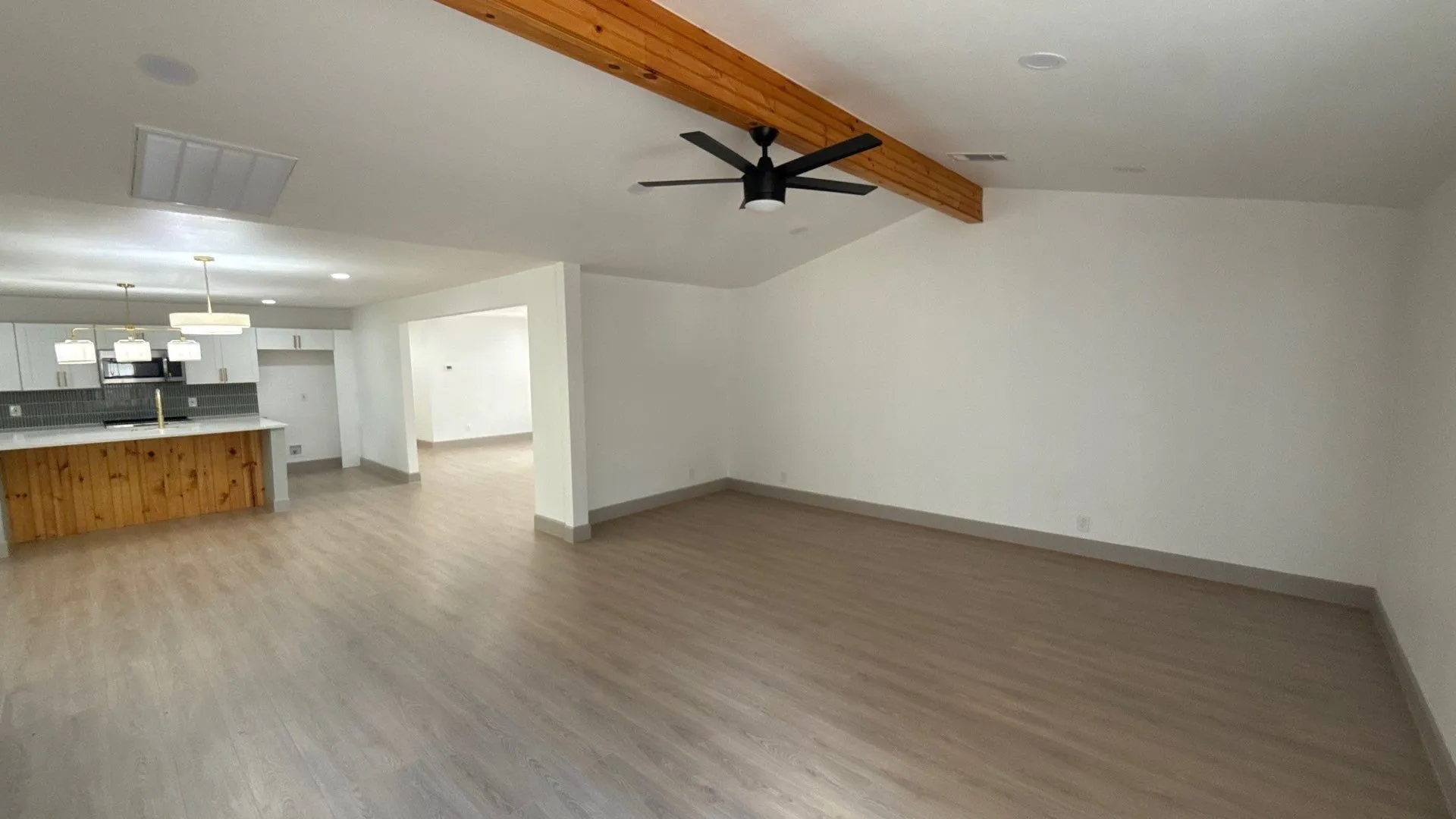 Open-concept interior featuring wood-finish flooring, a vaulted ceiling with an exposed wood beam, a matte black ceiling fan, recessed lighting, and a kitchen island with built-in wood cabinetry