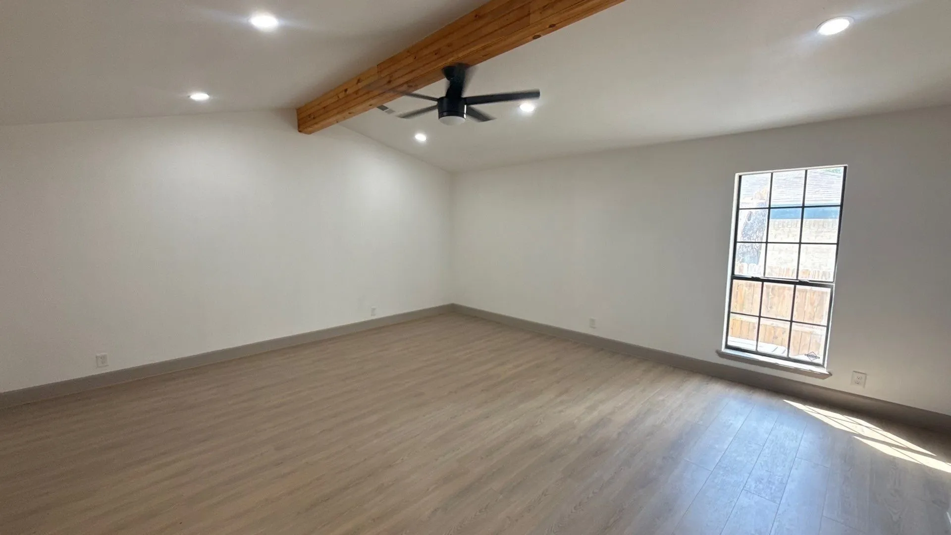 Vaulted ceiling featuring an exposed wood-finish beam, wood-finish flooring, recessed lighting, and a multi-pane window