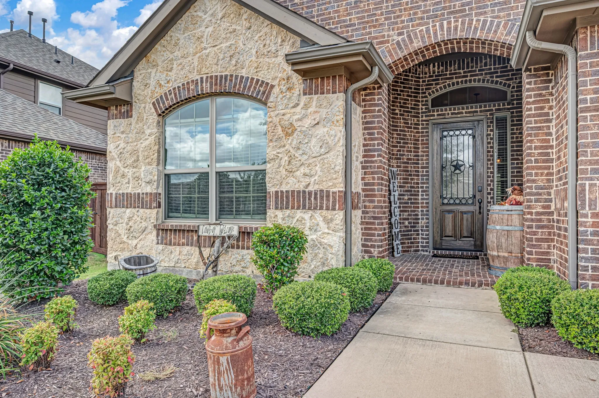 Exterior facade featuring textured stone veneer and brick masonry, arched entryway with a decorative iron-insert door, and concrete walkway