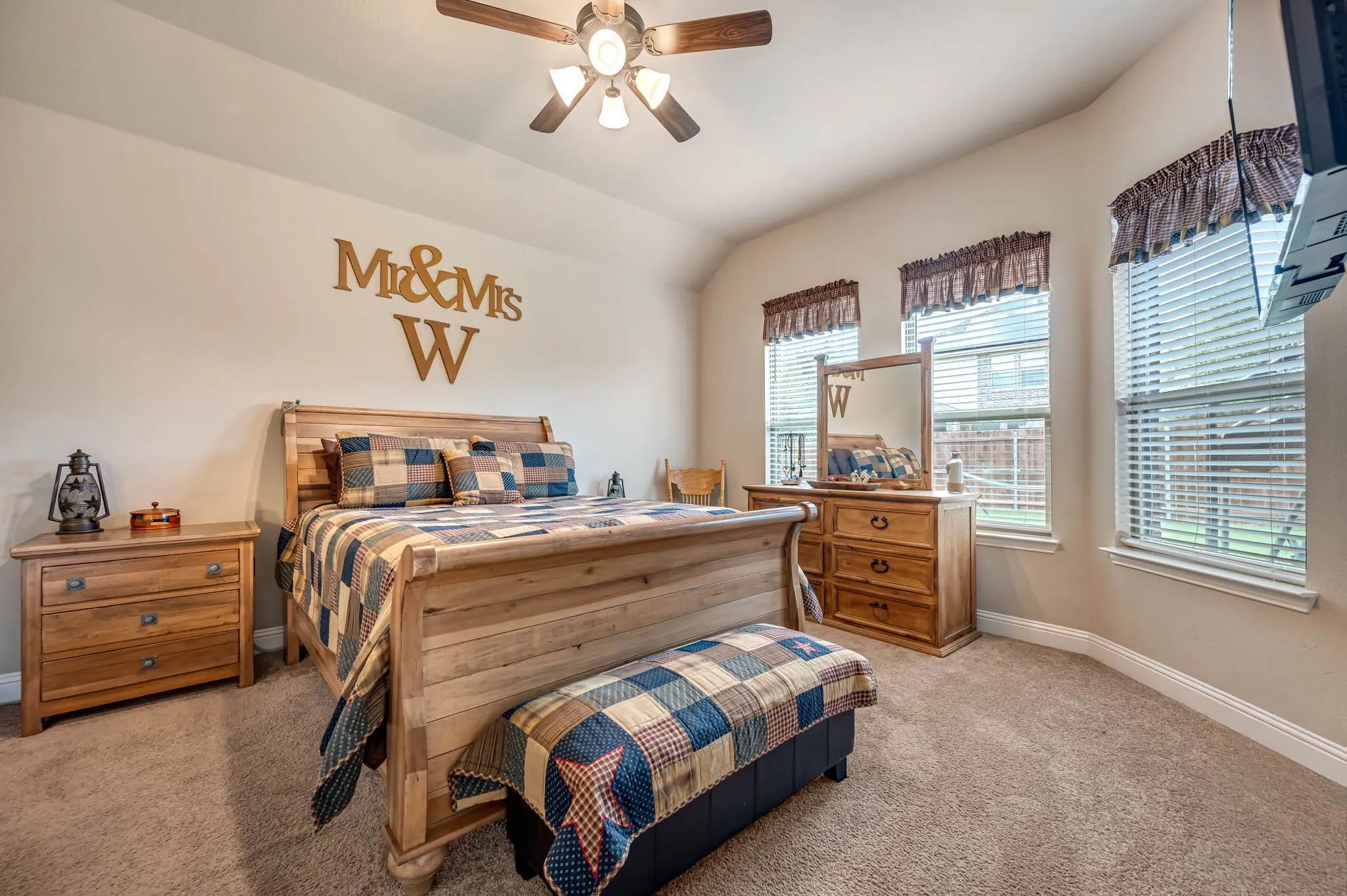 Neutral-toned interior room featuring vaulted ceilings, carpeted flooring, a multi-blade ceiling fan with integrated lighting, and multiple windows with horizontal blinds