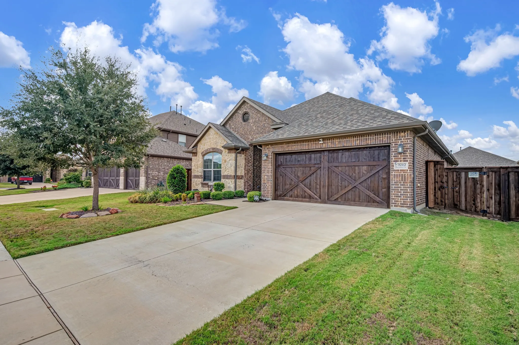 Brick and stone veneer exterior featuring a dual-bay garage with carriage-style wood-finish doors, a concrete driveway, and professional landscaping
