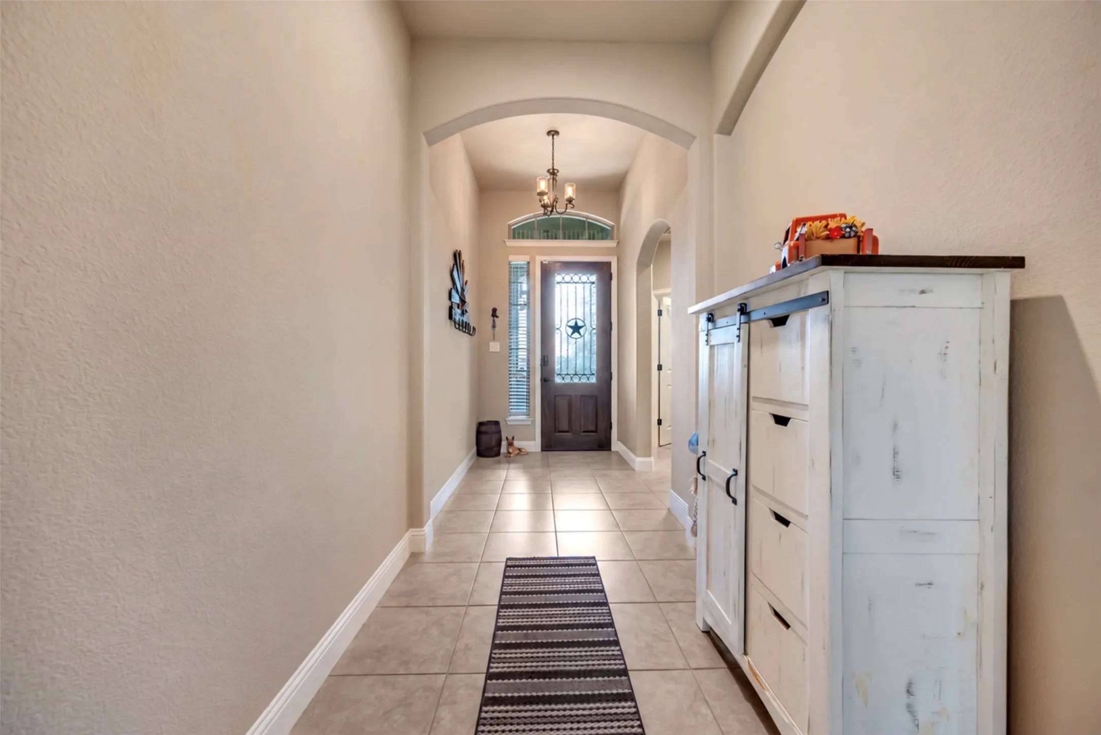Foyer featuring large-format ceramic tile flooring, arched architectural detailing, high ceilings, an iron-accented front door, and a transom window