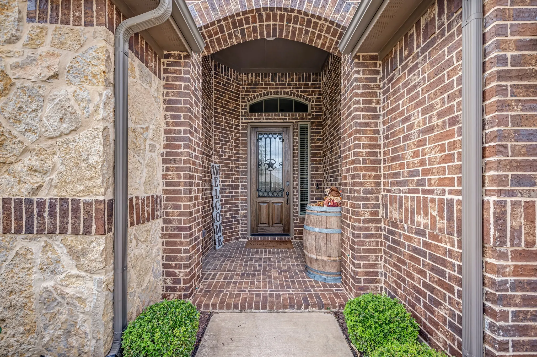 Brick exterior facade featuring a stone veneer accent, arched entryway, and a solid wood front door with decorative metal insert