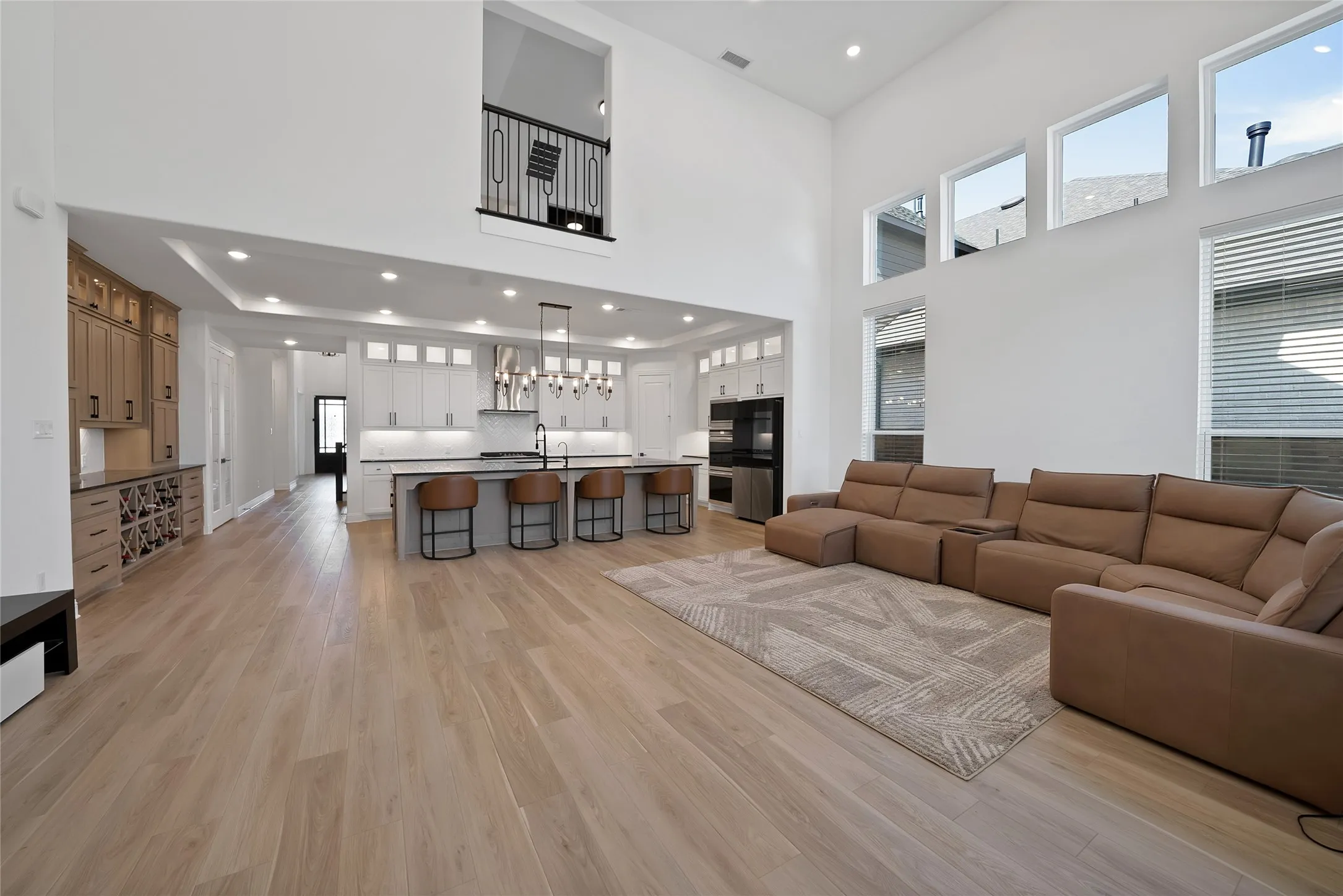 Double-height living area featuring floor-to-ceiling windows, wood-finish flooring, a kitchen island with seating, built-in cabinetry, and a mezzanine overlook with metal railing