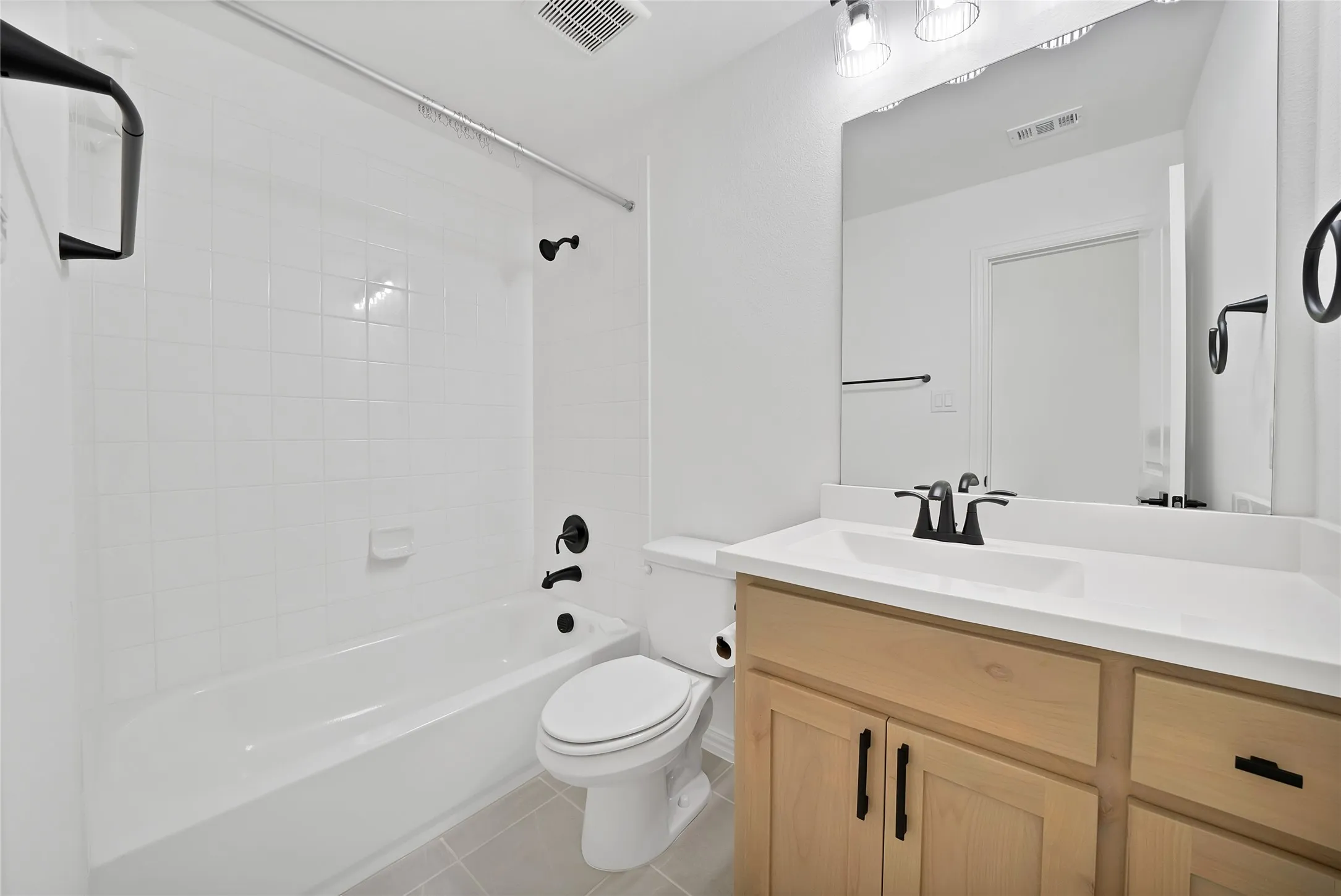 Bathroom featuring a vanity with light wood-finish cabinetry, a solid surface countertop, matte black hardware, and a tile-surround shower and tub combination