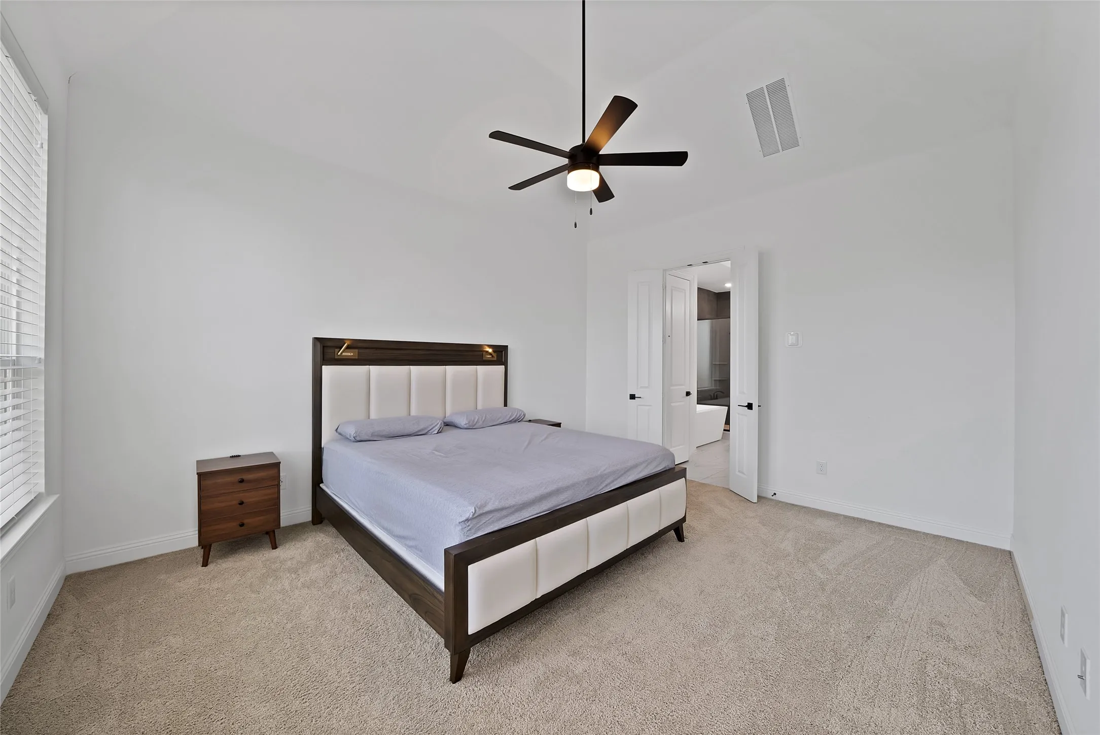 Vaulted ceiling featuring a central matte black ceiling fan with an integrated light fixture, neutral wall-to-wall carpeting, and double-door entry