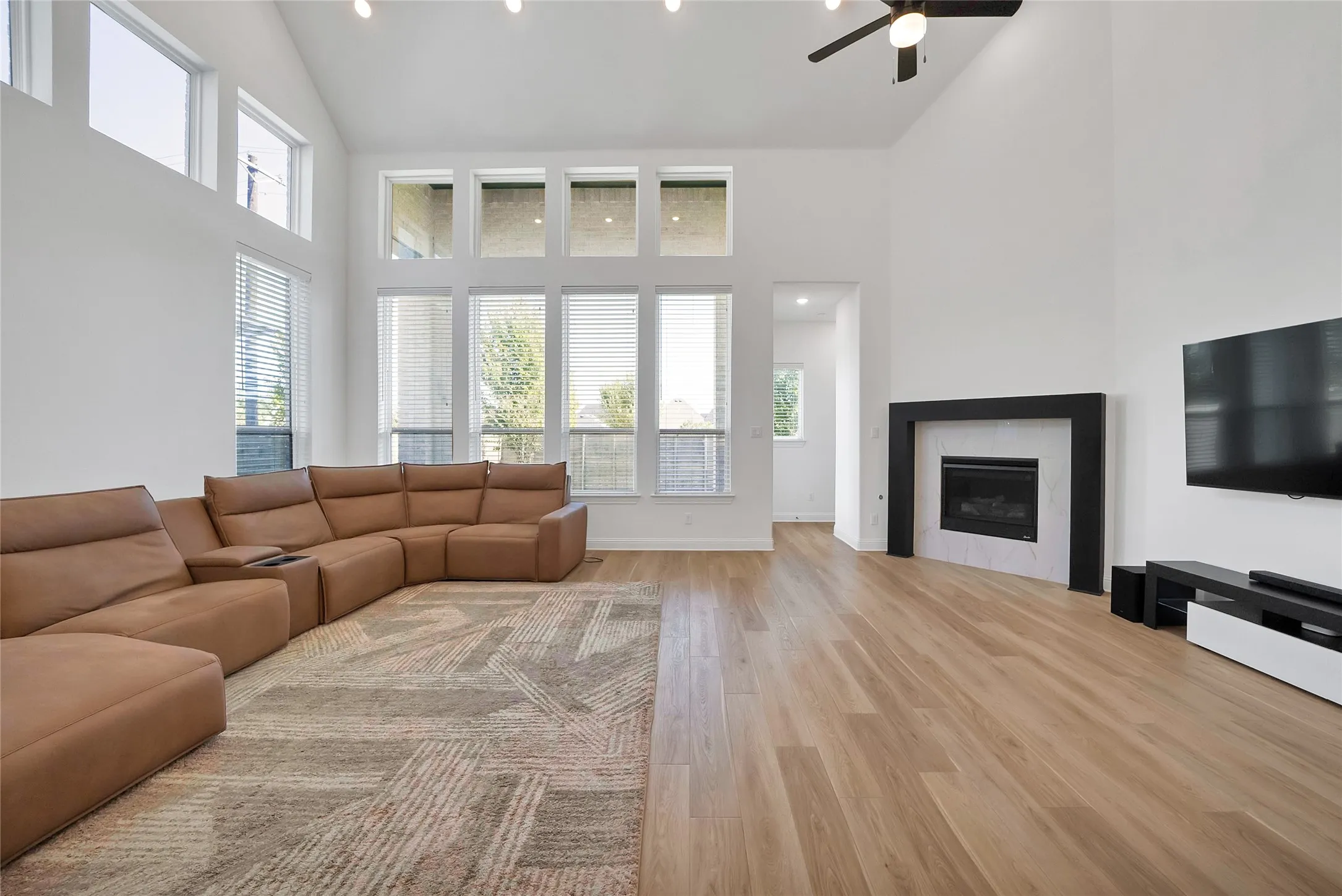 Vaulted ceilings with large-format windows, wood-finish flooring, and a fireplace featuring a black mantel and white stone surround
