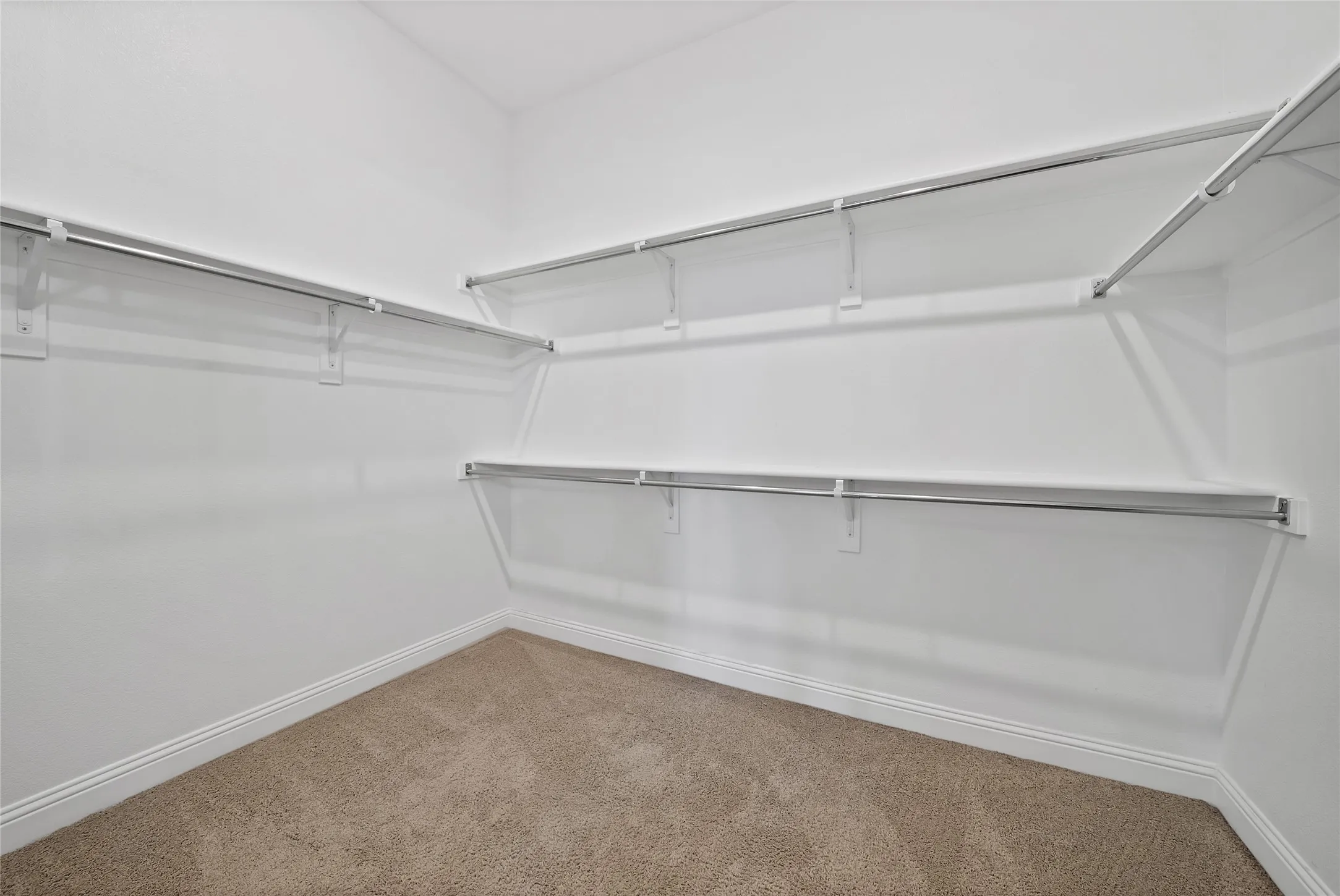 Walk-in closet featuring neutral carpeting and tiered metal shelving units with integrated garment rods