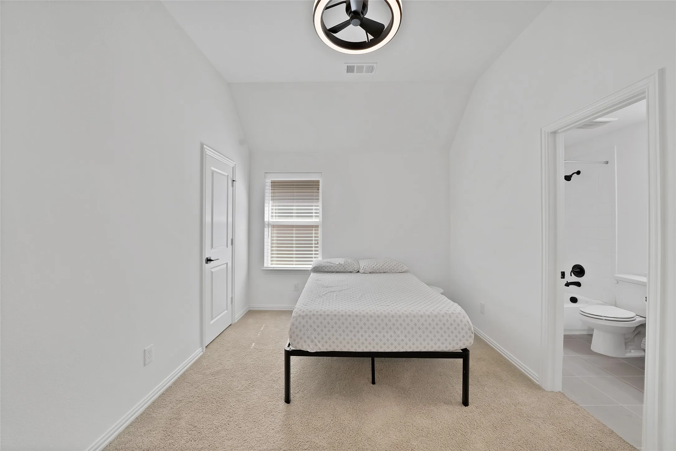 Vaulted ceiling featuring a contemporary circular flush-mount light fixture, neutral wall-to-wall carpeting, and a private bath entry