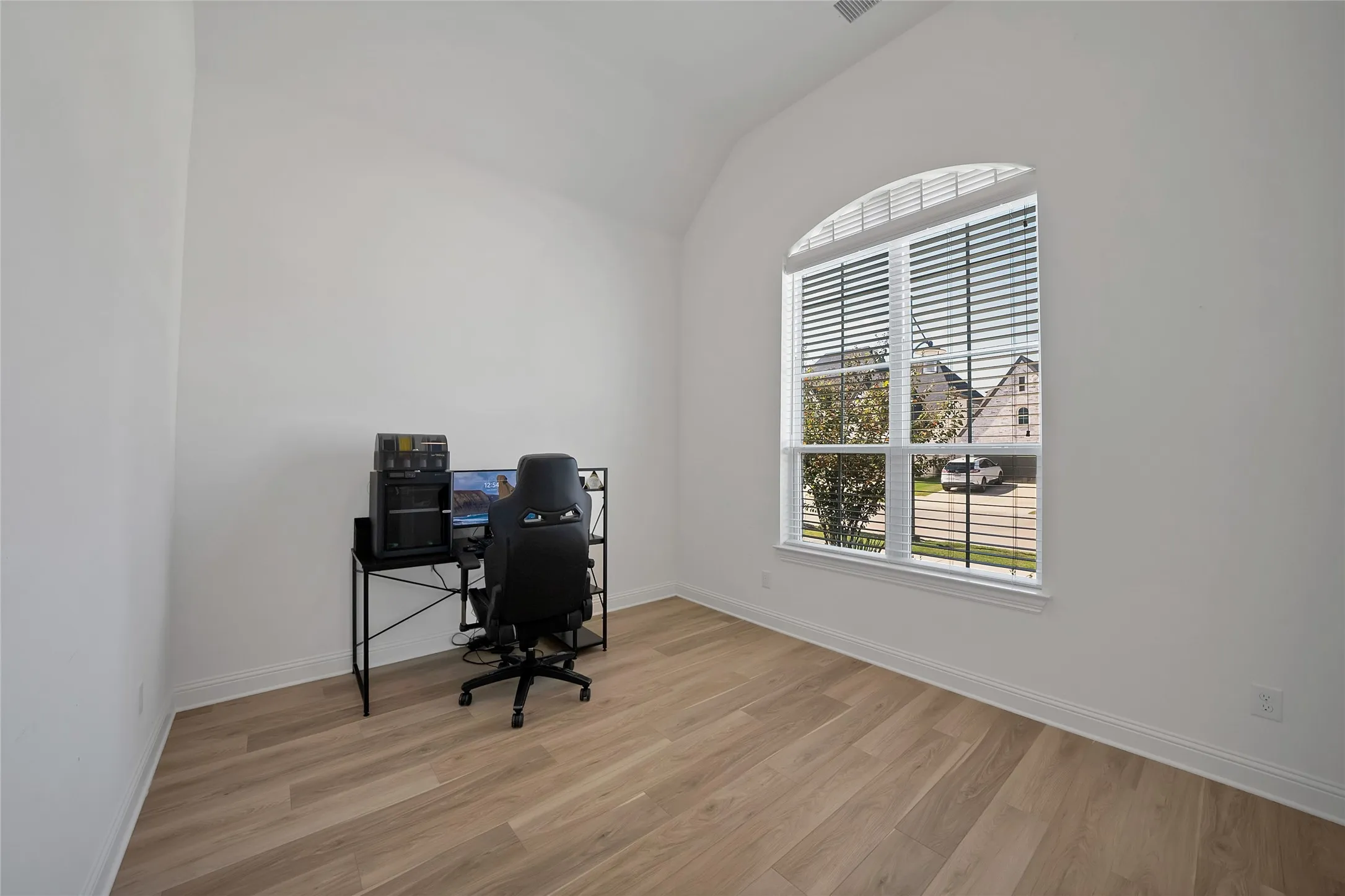 Room featuring wood-finish flooring, vaulted ceilings, and a tall window with an arched transom